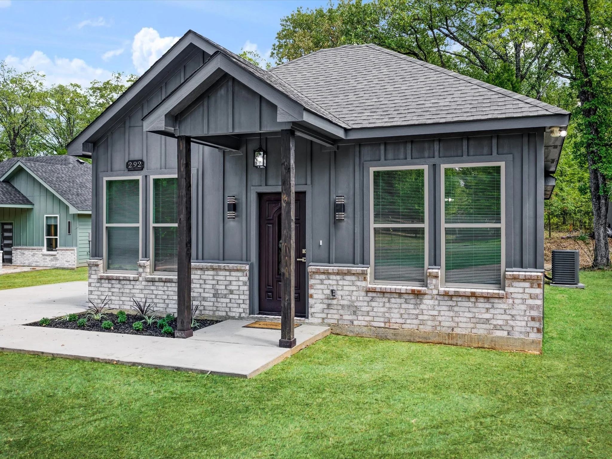 Modern exterior featuring vertical siding, a covered porch with substantial columns, a brick facade, and an asphalt shingle roof