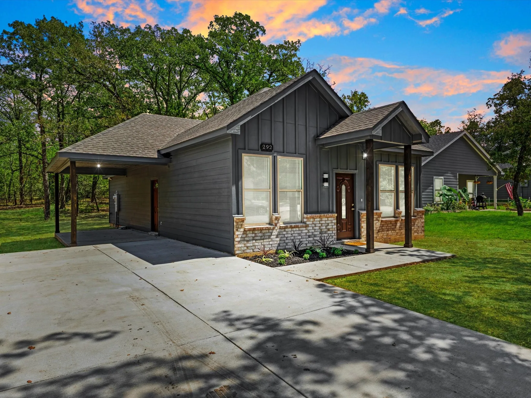 Exterior featuring dark gray siding, stone veneer accents, an attached covered carport, a covered front porch with wood-finish columns, and a concrete driveway