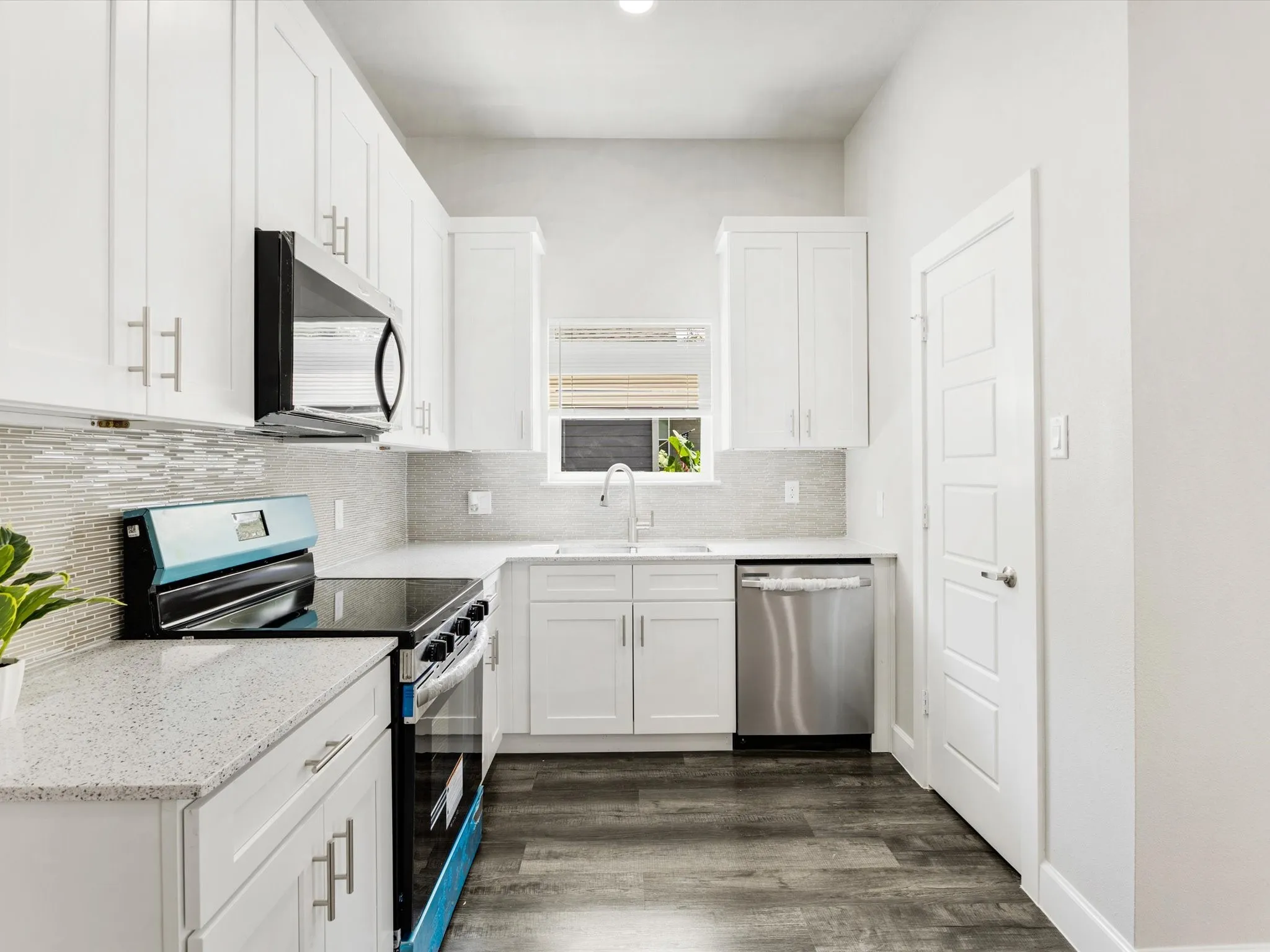 White cabinetry with brushed nickel hardware, light-toned countertops, a mosaic tile backsplash, a stainless steel dishwasher, and wood-finish flooring
