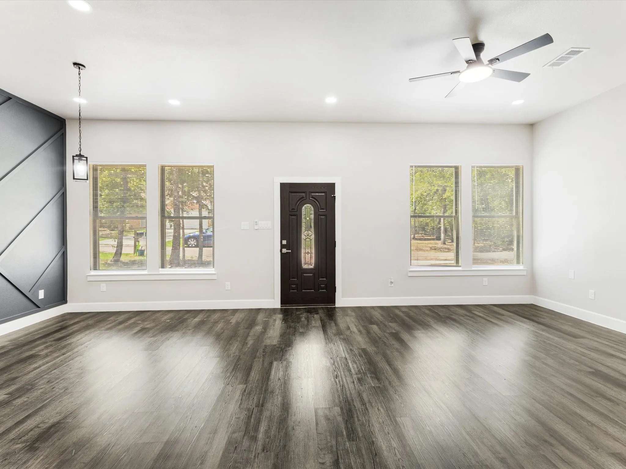 Wood-finish flooring throughout, modern ceiling fan, recessed lighting, decorative accent wall, and a detailed front entry door