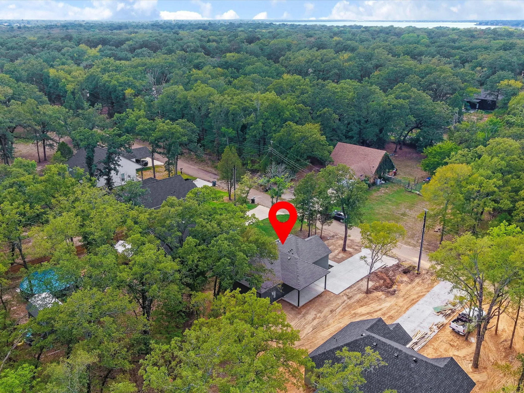 Expansive treed lot featuring a newly constructed residence with a dark shingled roof, a concrete driveway, and surrounding mature trees