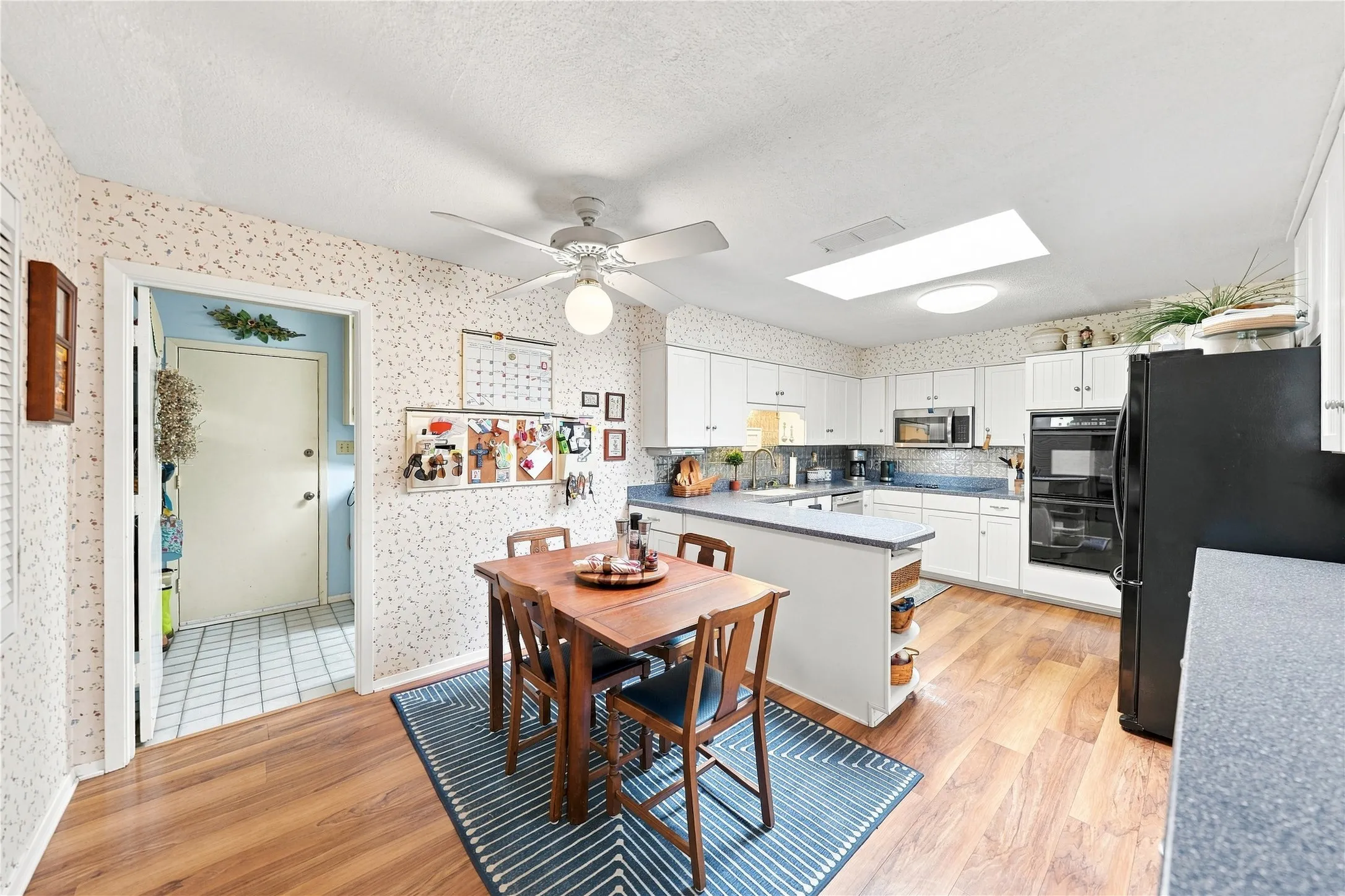 Kitchen featuring white cabinetry, built-in double ovens, a skylight, wood-finish flooring, and a ceiling fan