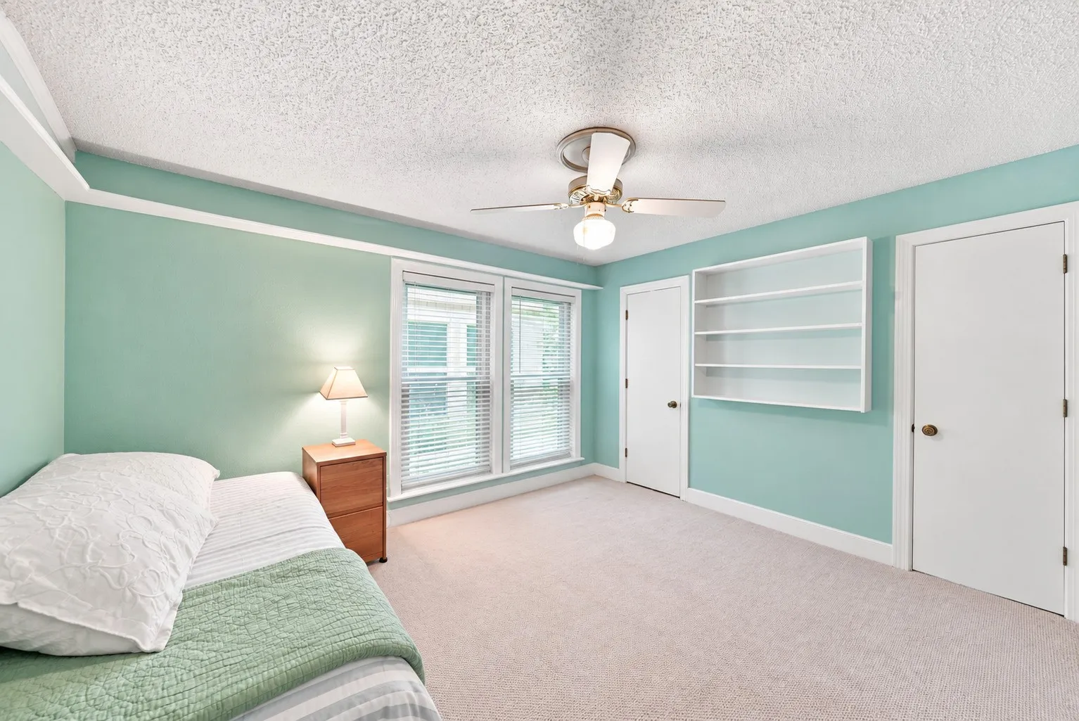 Plush carpeting, multiple windows with blinds, built-in shelving, and a ceiling fan