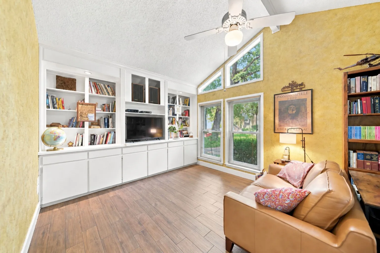 Vaulted ceilings with a ceiling fan, wood-finish flooring, custom built-in cabinetry, and multiple windows