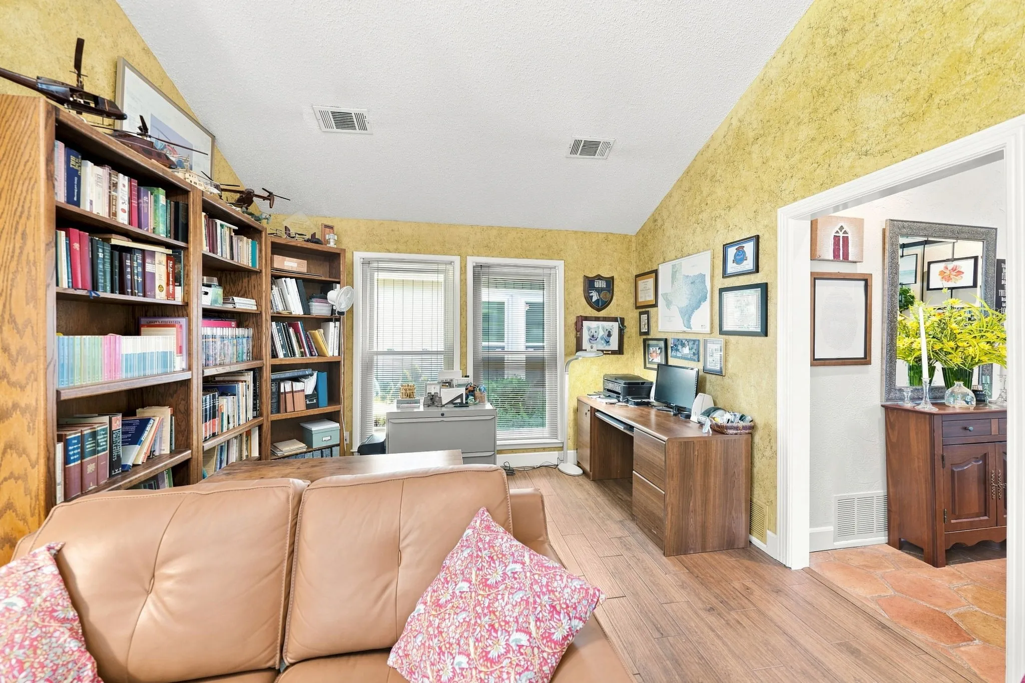 Vaulted ceiling with textured wall finish, wood-finish flooring, built-in wood bookcases, and a large window with vertical blinds