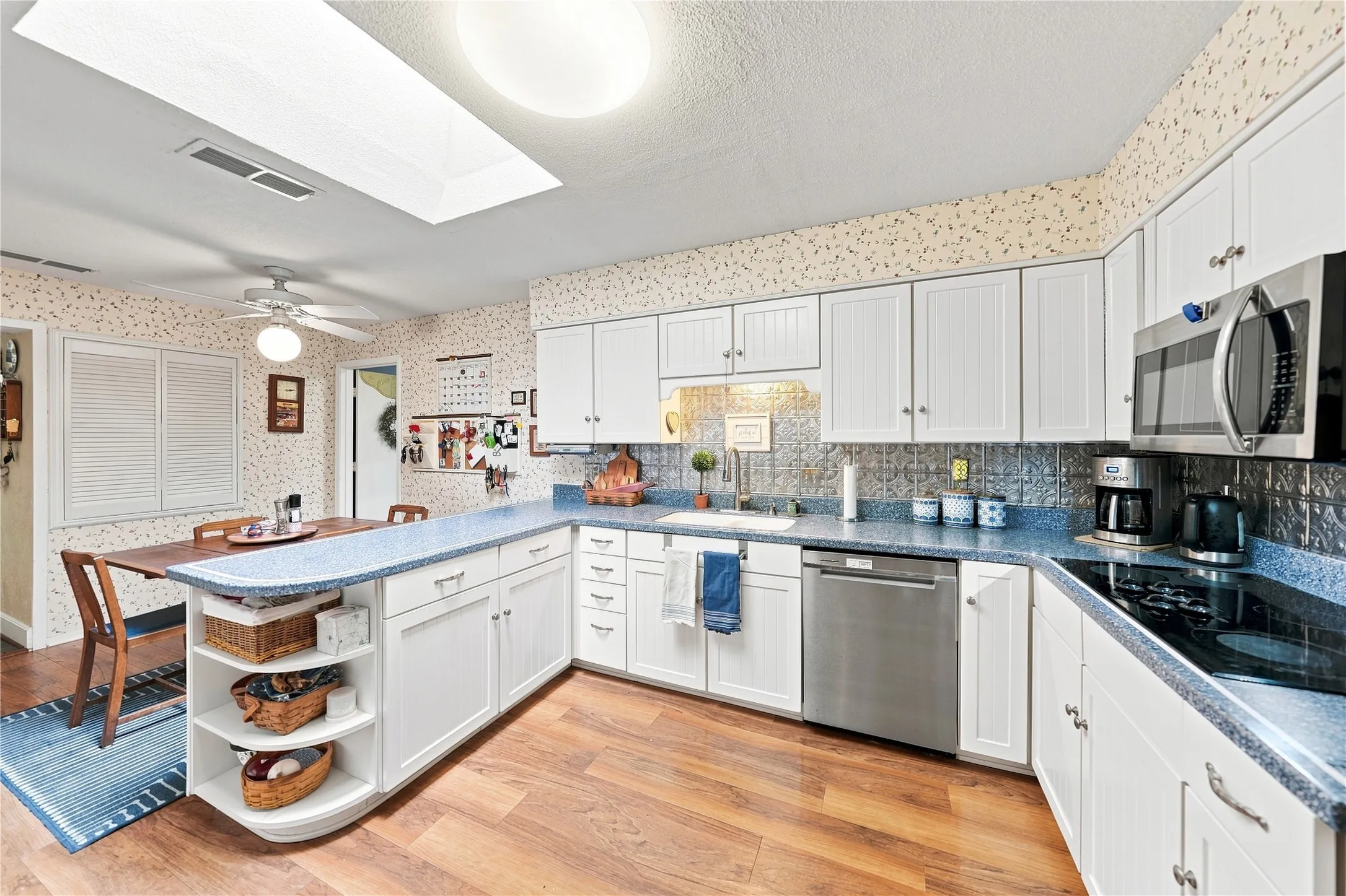 Kitchen featuring wood-finish flooring, white cabinetry, a skylight, stainless steel appliances, and a built-in cooktop