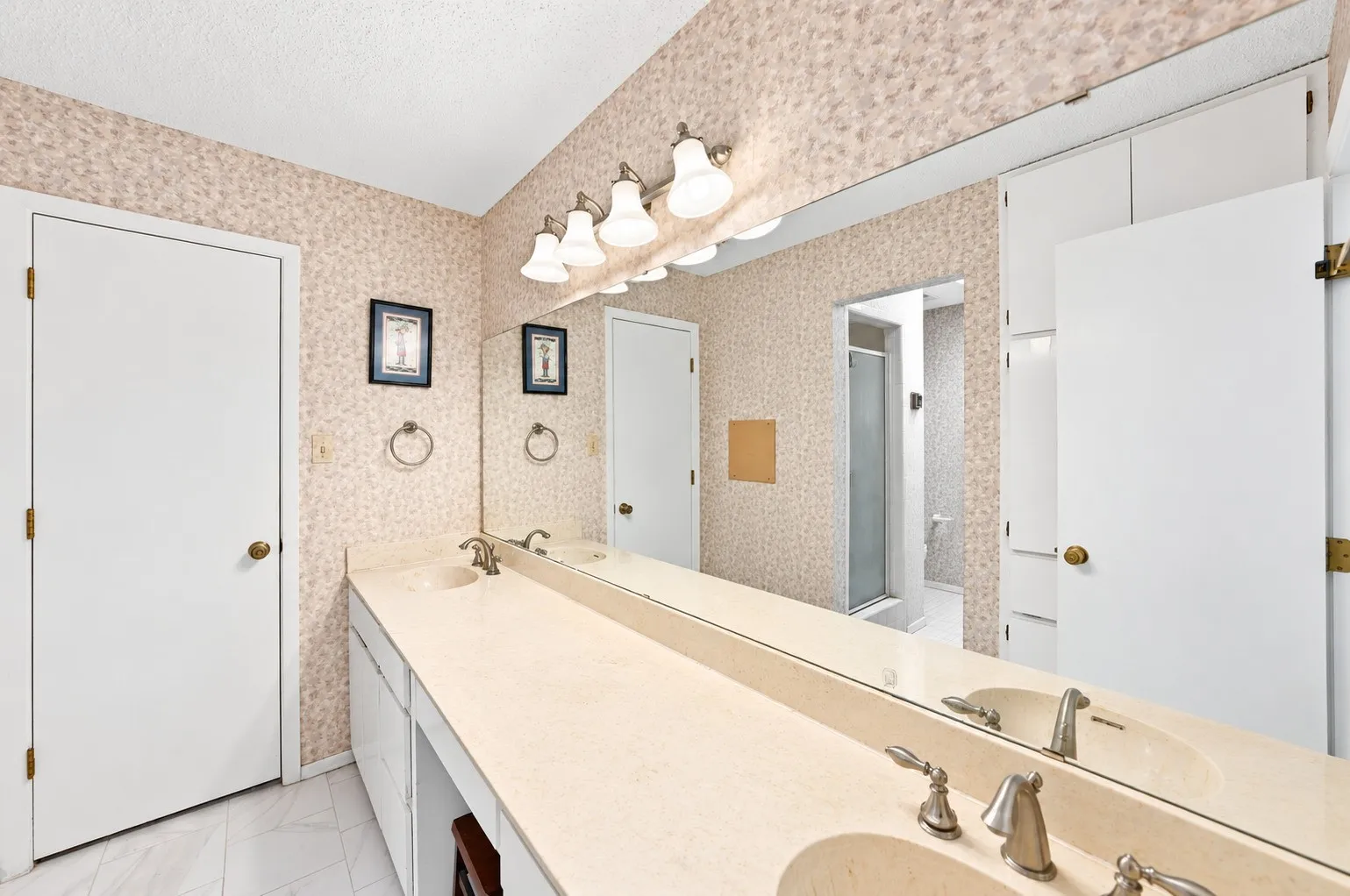 Dual integrated sinks with brushed nickel fixtures, an expansive vanity, full-width mirror, overhead vanity lighting, and built-in storage cabinetry