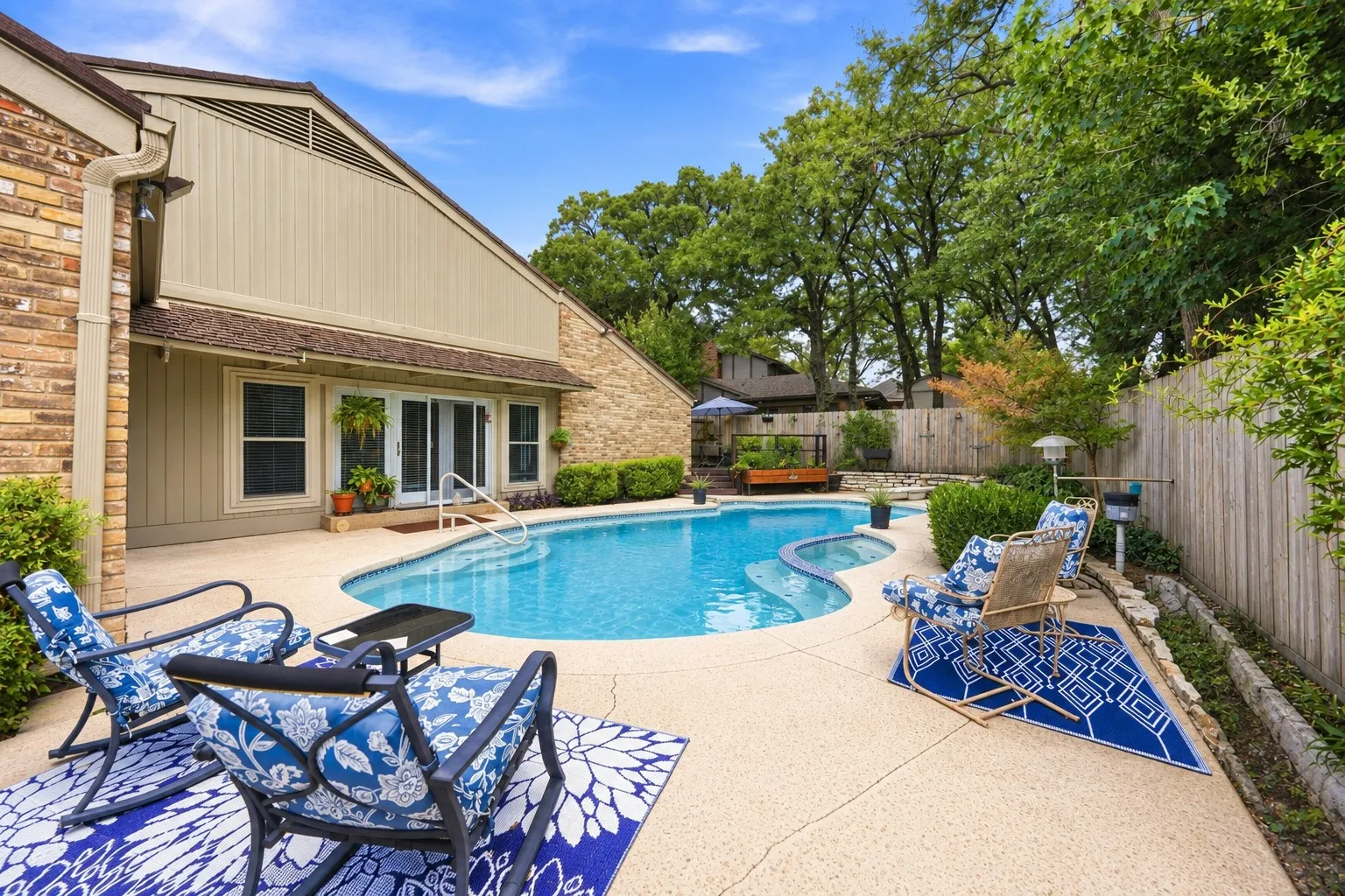 Backyard oasis featuring a freeform swimming pool, extensive concrete patio, and mature perimeter landscaping