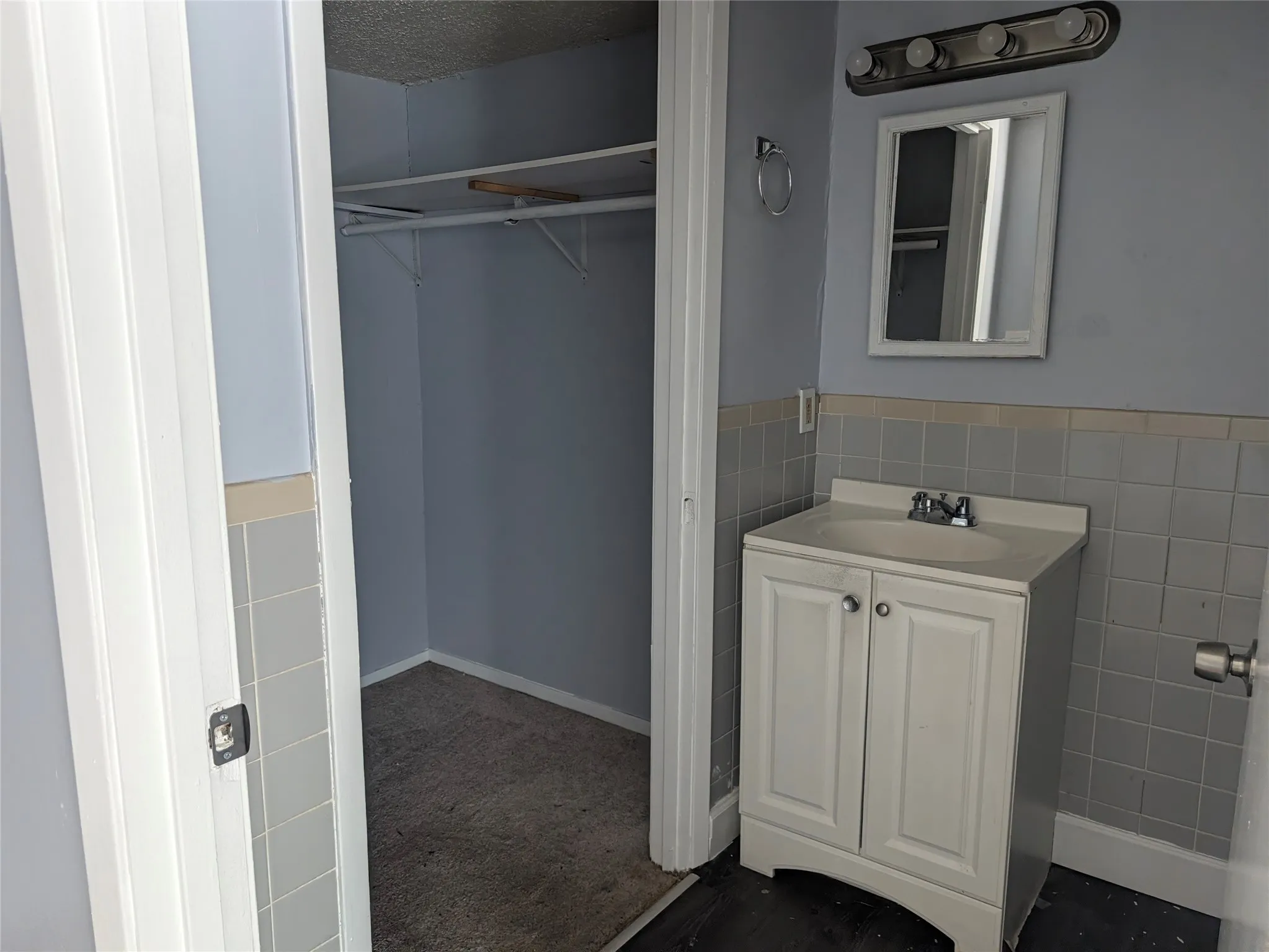 White vanity with integrated sink, rectangular mirror, and a four-bulb vanity light fixture