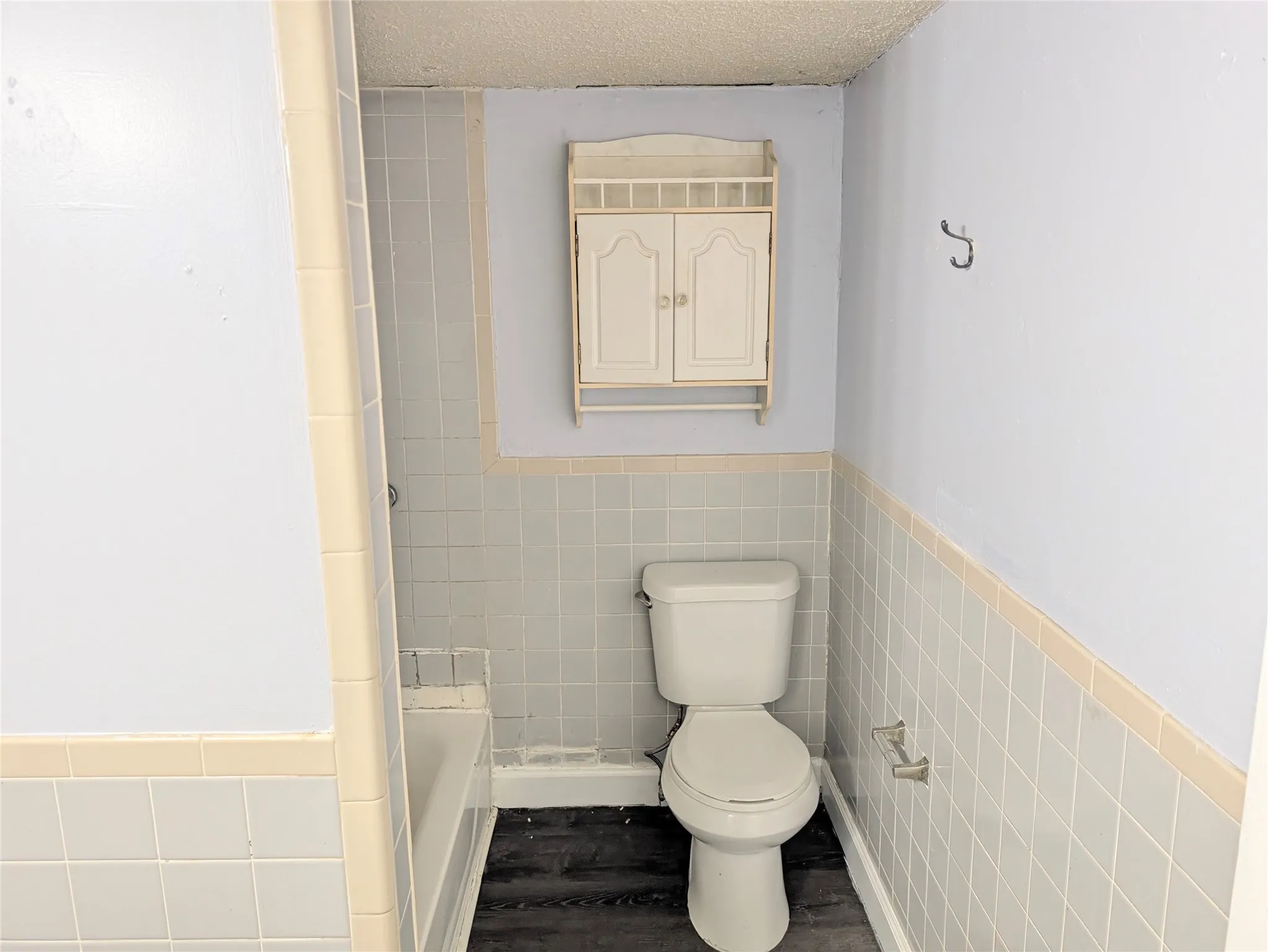 Wall-mounted cabinet with dual doors, tiled walls, and textured ceiling