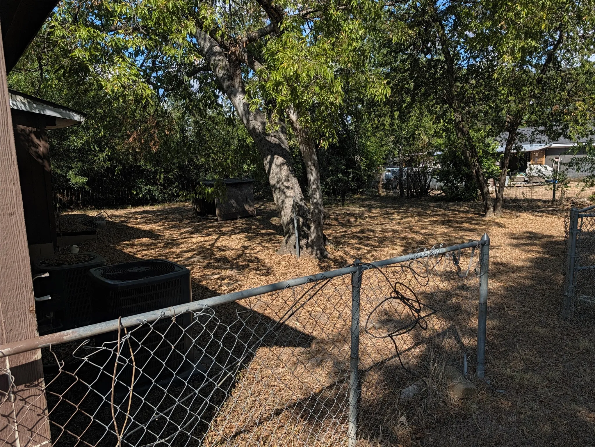 Fenced yard with mature trees providing shade and an area of wood chip ground cover