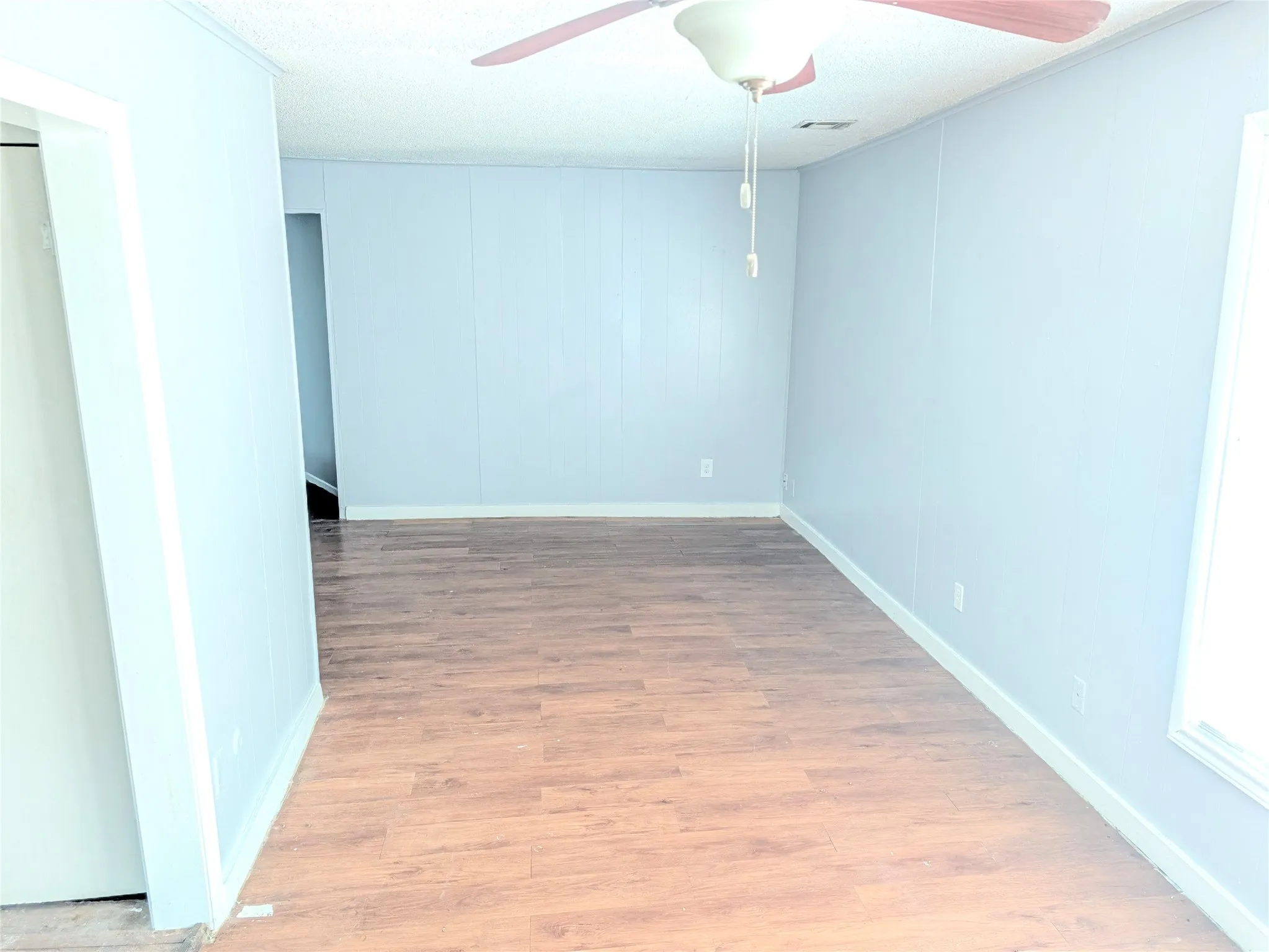 Wood-finish flooring with light blue wall paneling, white trim, and a ceiling fan