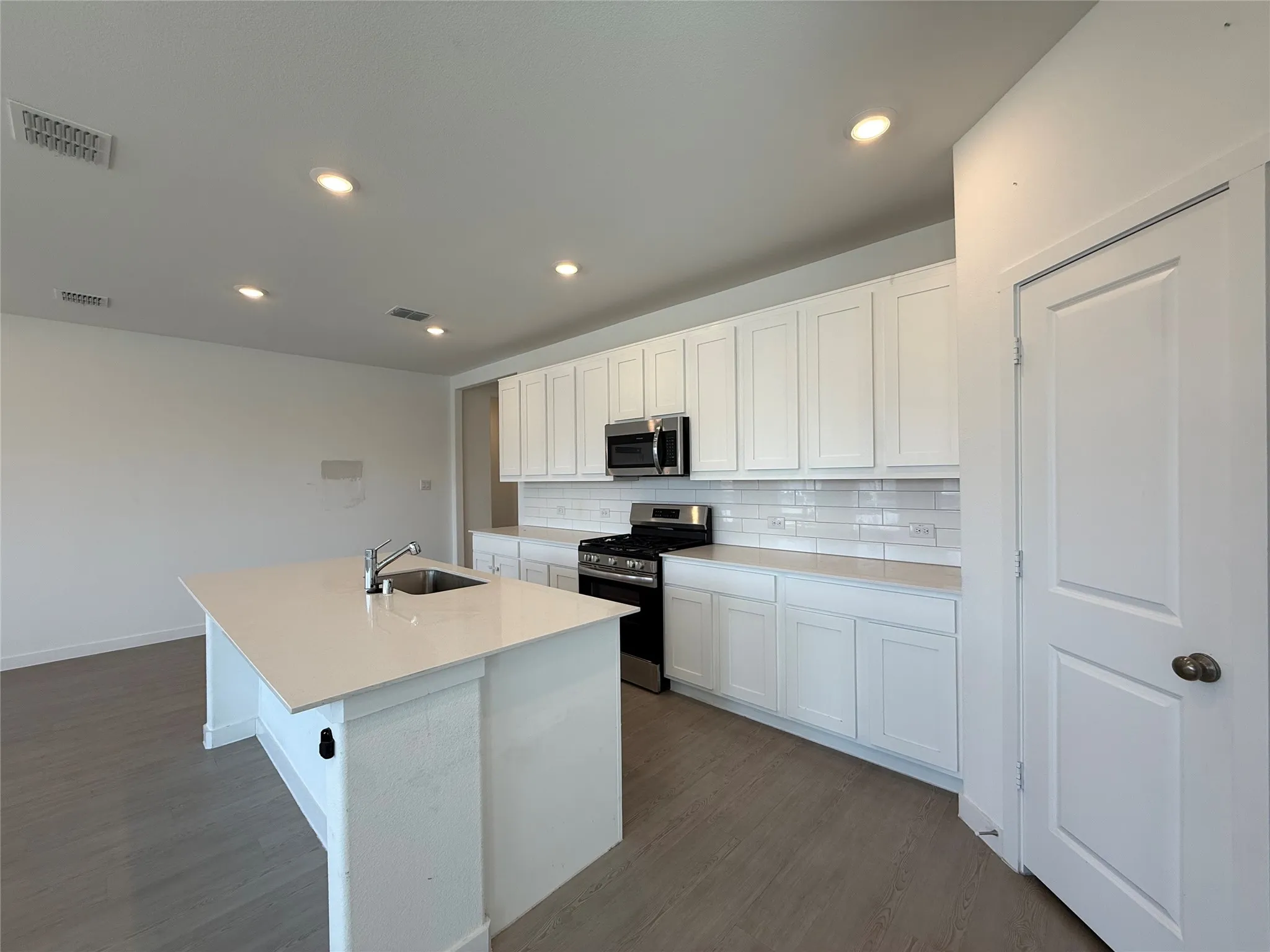 Kitchen featuring white cabinetry, subway tile backsplash, stainless steel appliances, a center island with sink, and wood-finish flooring