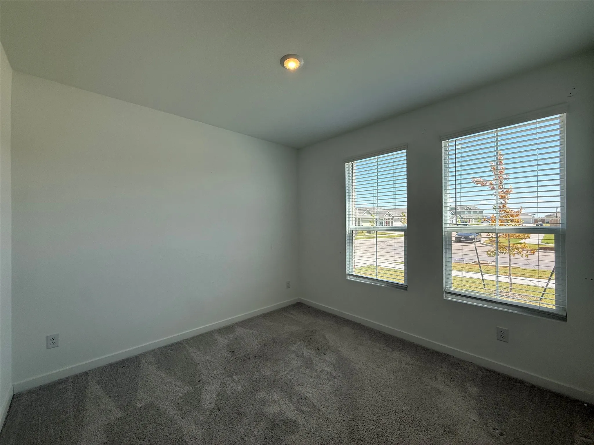 Recessed ceiling lighting, two windows with blinds, light gray wall paint, and gray carpet flooring