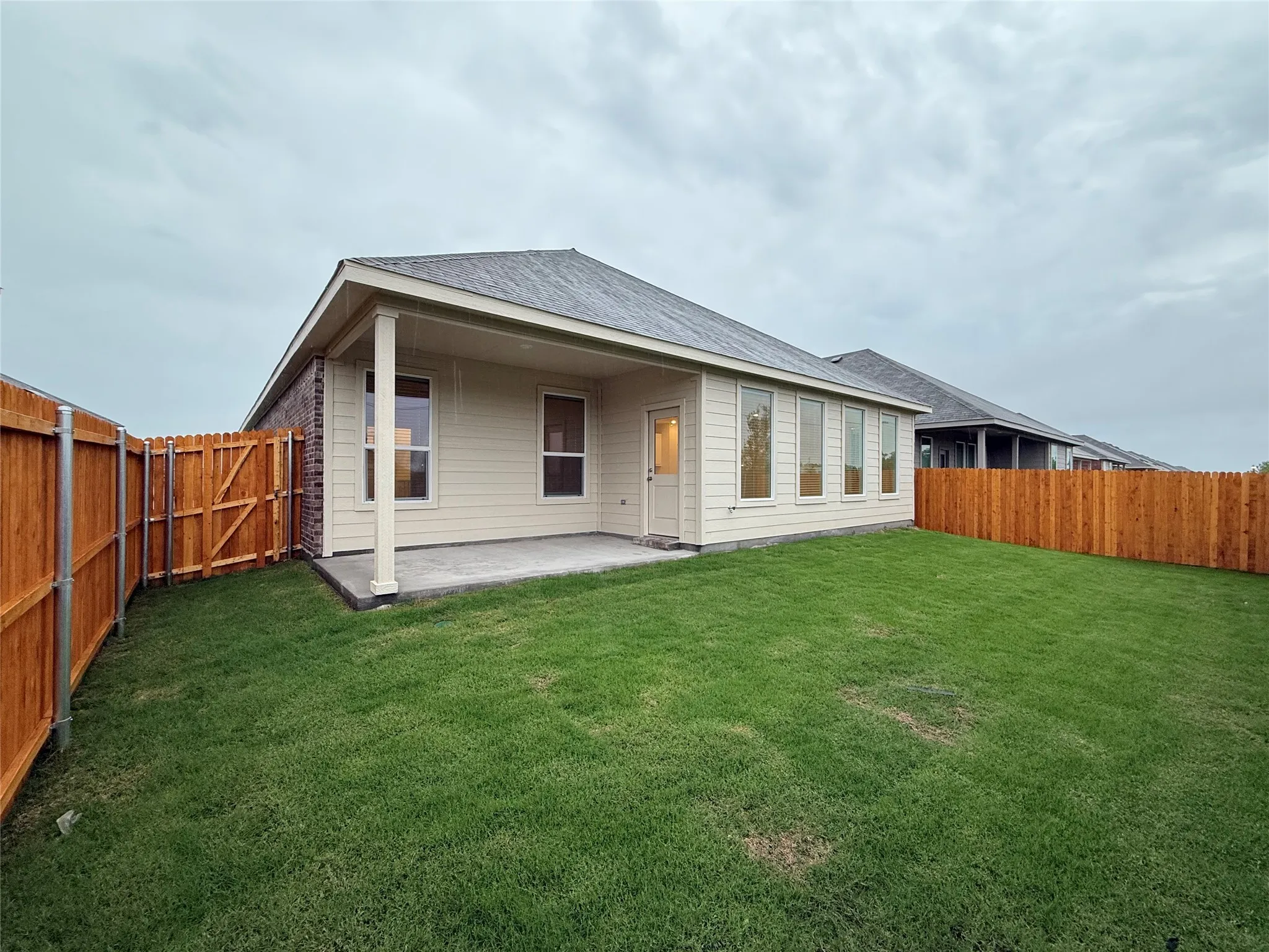 Expansive backyard featuring a covered patio, wood privacy fencing, and a brick and siding exterior