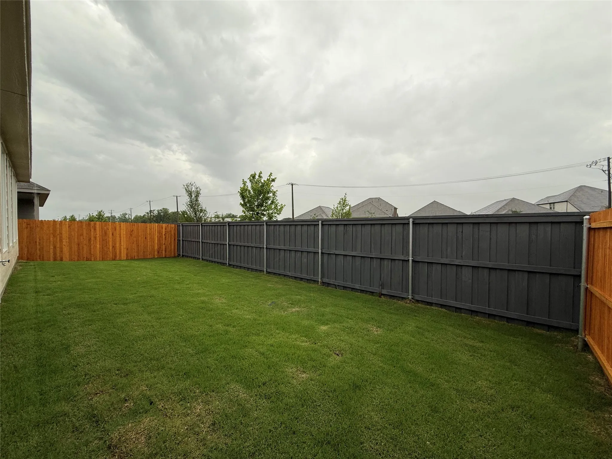 Expansive backyard with a manicured lawn, featuring a wood privacy fence and a dark-stained privacy fence