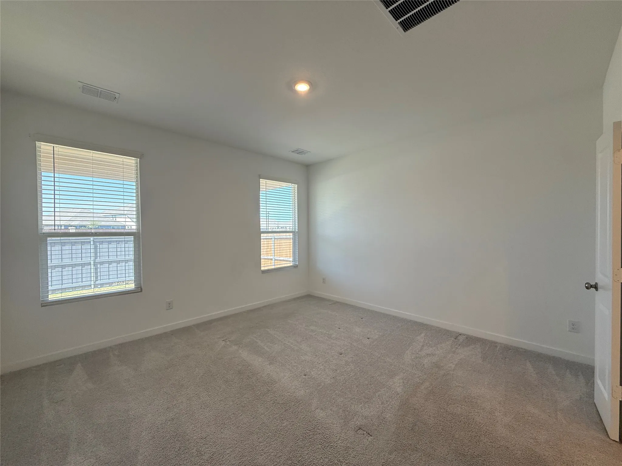 Neutral wall color, recessed ceiling light, and two windows with horizontal blinds