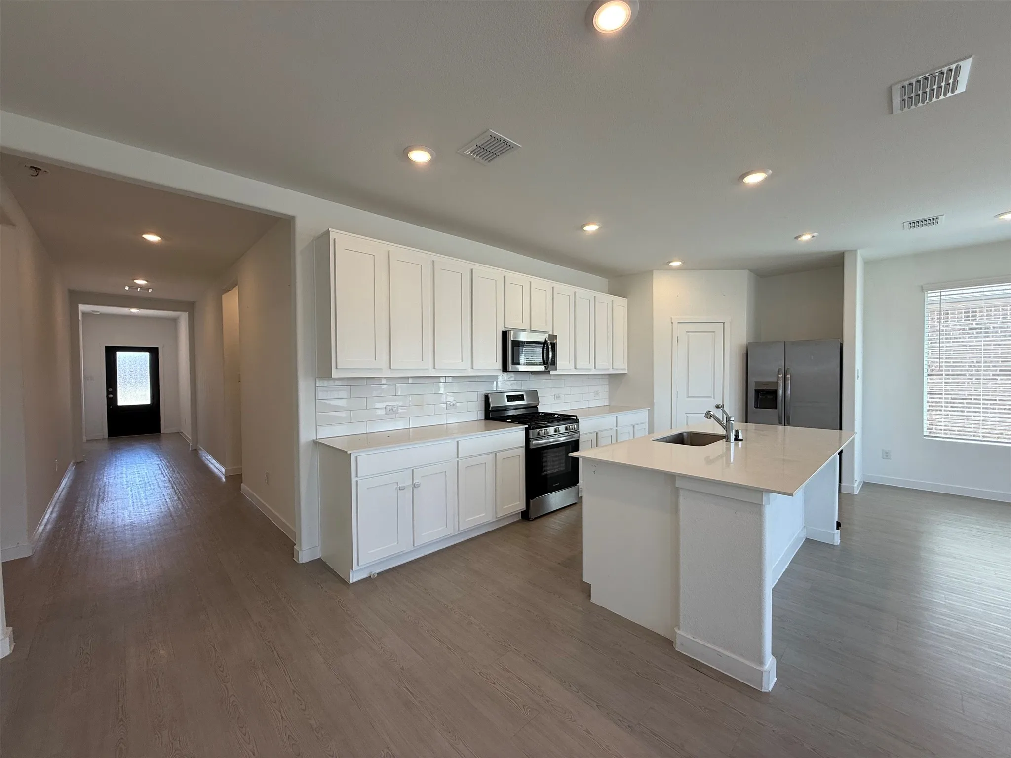 Kitchen featuring an island with an undermount sink, white cabinetry, stainless steel appliances, and subway tile backsplash