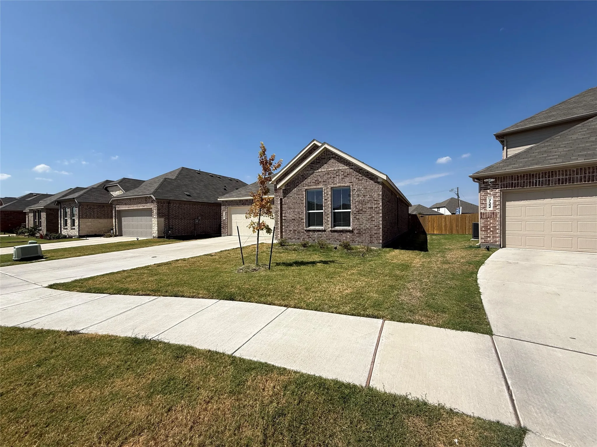 Brick exterior with multiple windows, attached garage, concrete driveway, and a partially fenced backyard