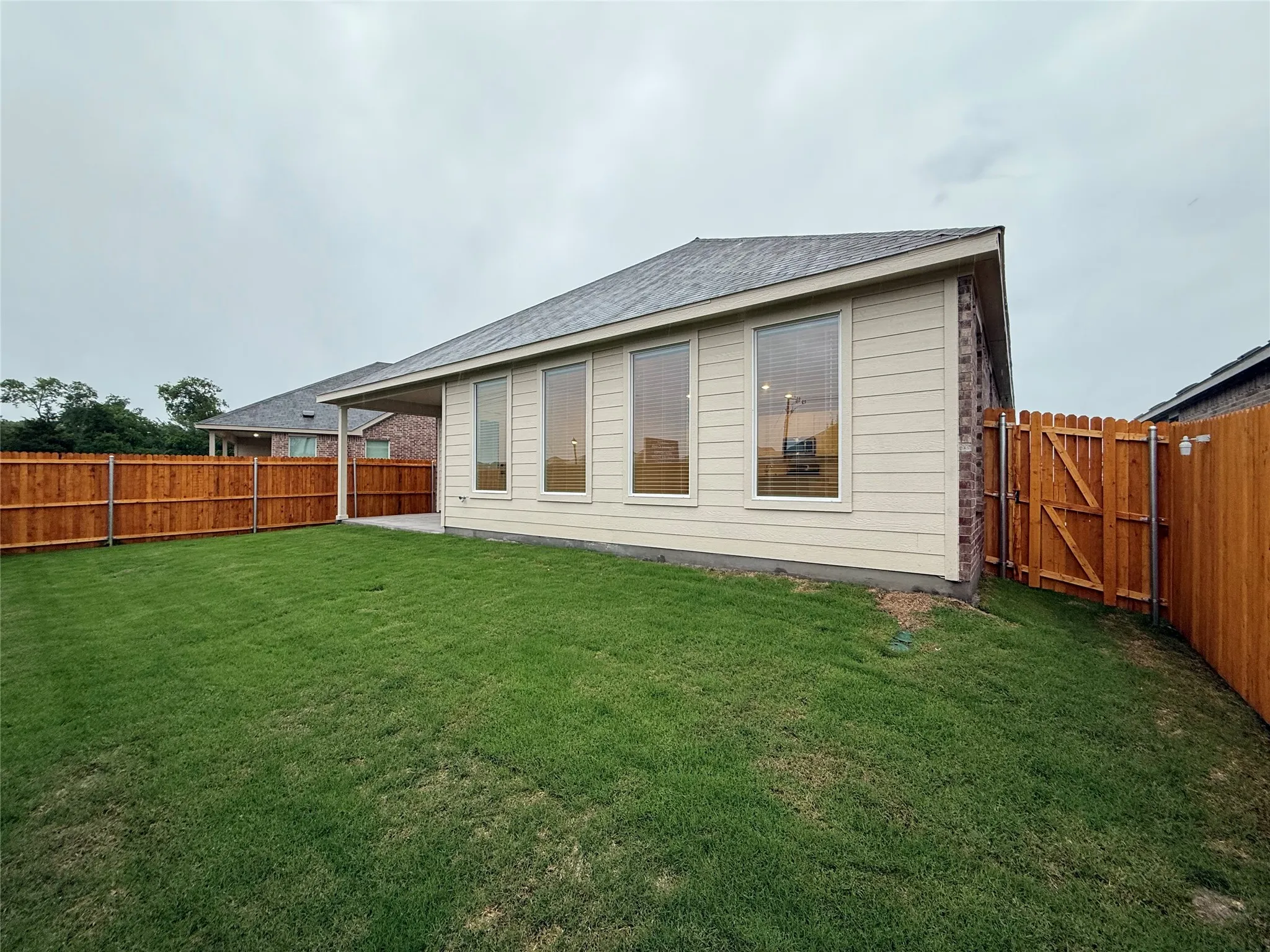 Expansive fenced backyard with a manicured lawn, covered patio, and multiple large windows