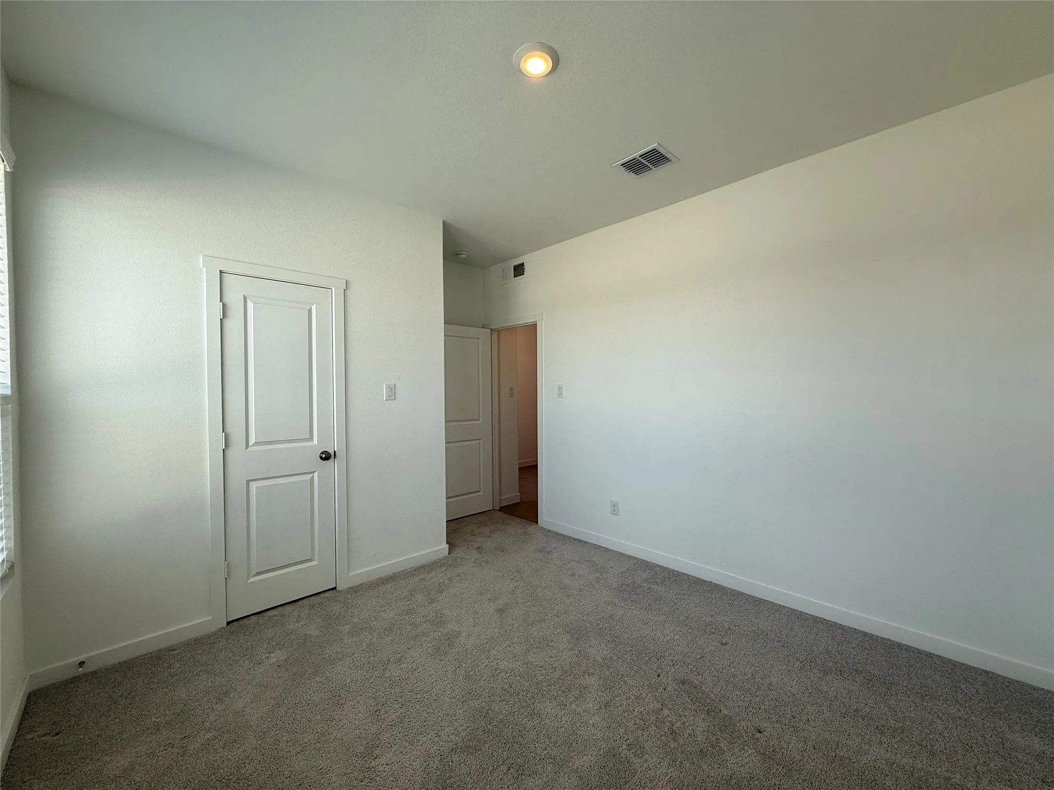 Neutral wall tones, plush carpeting, recessed ceiling lighting, and a paneled interior door