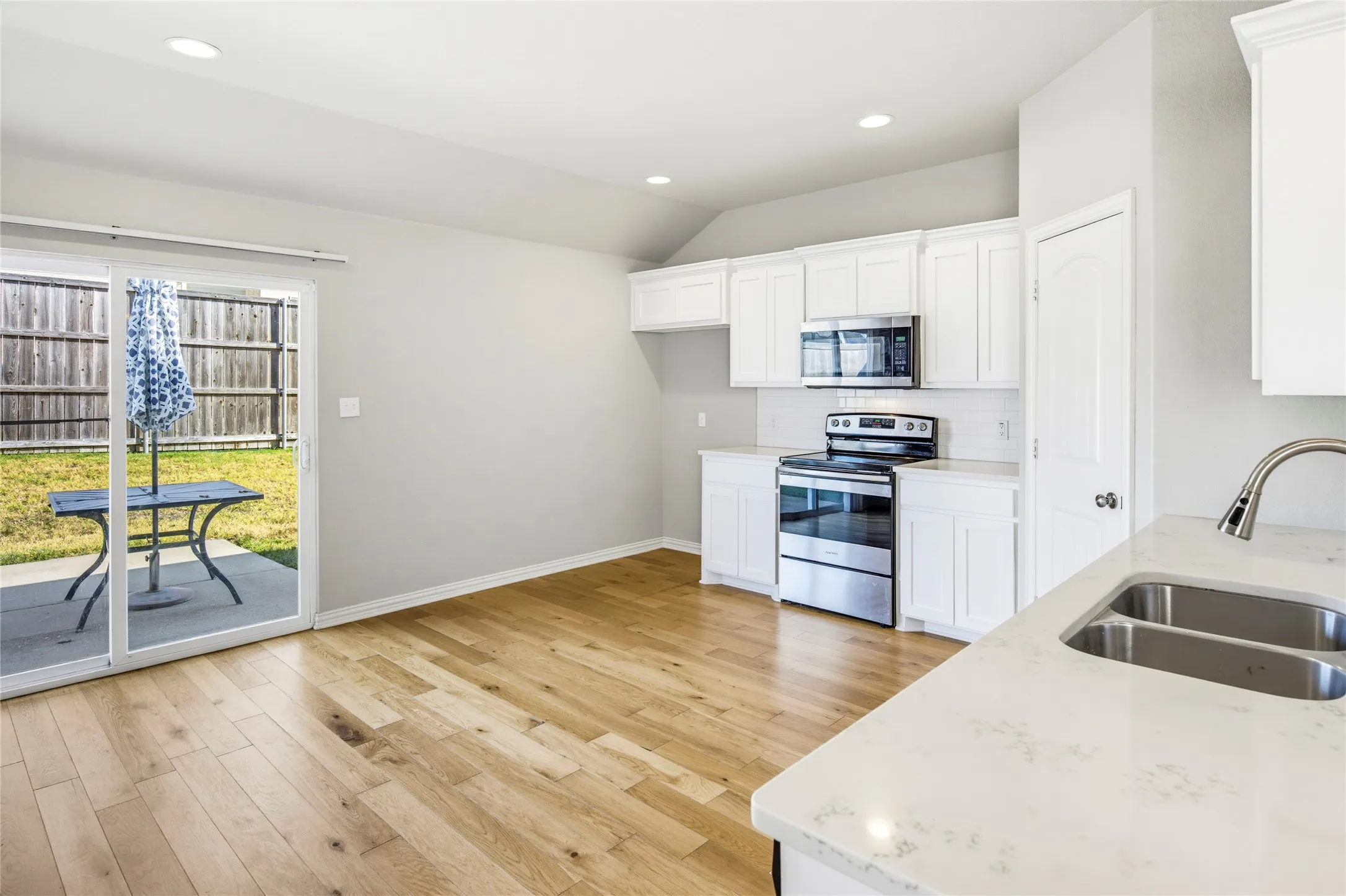 Kitchen featuring stainless steel appliances, white cabinetry, a dual basin sink, light-toned countertops, and wood-finish flooring