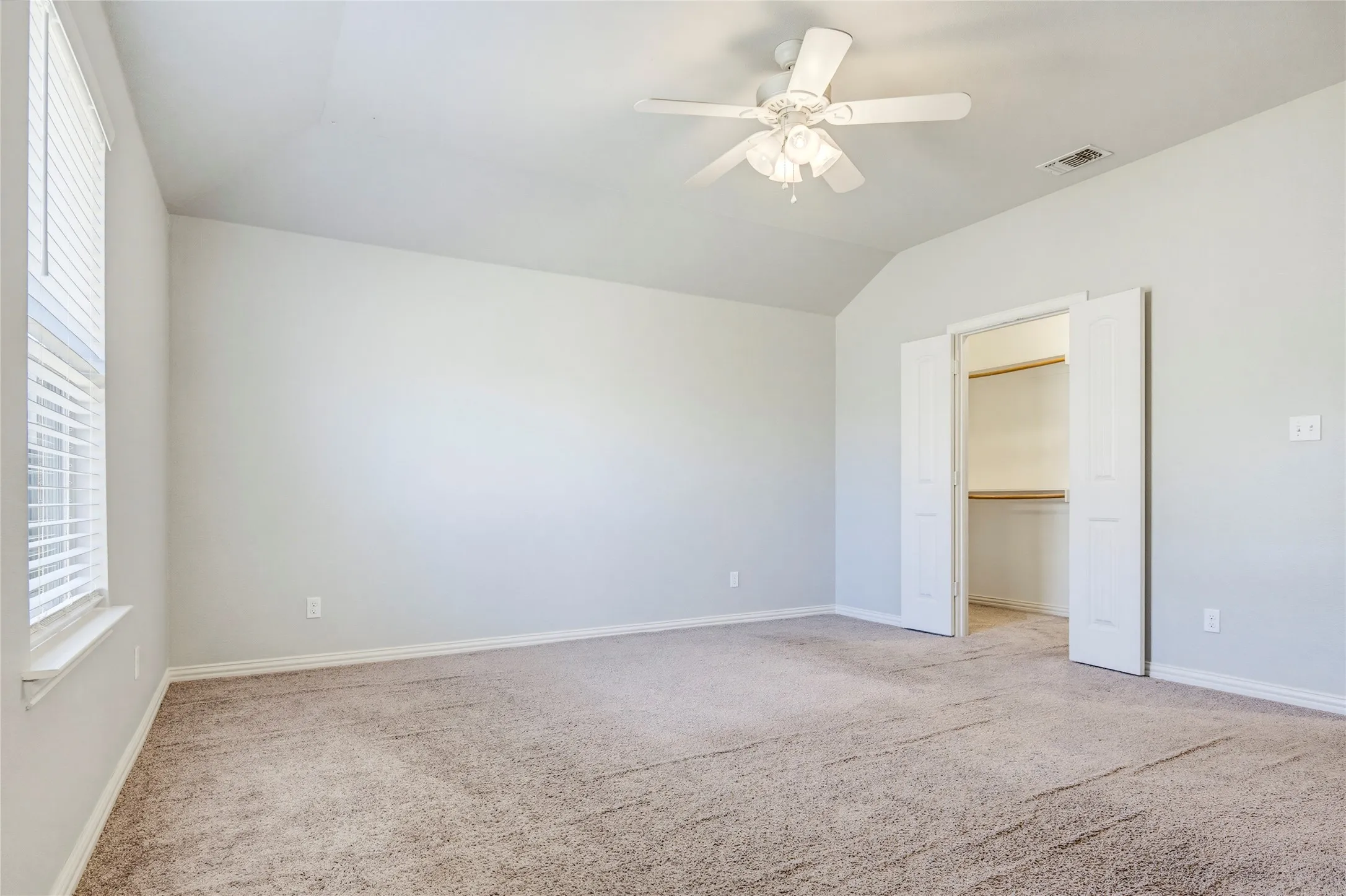 Vaulted ceiling with a ceiling fan, carpeted flooring, window with blinds, and a walk-in closet with bi-fold doors