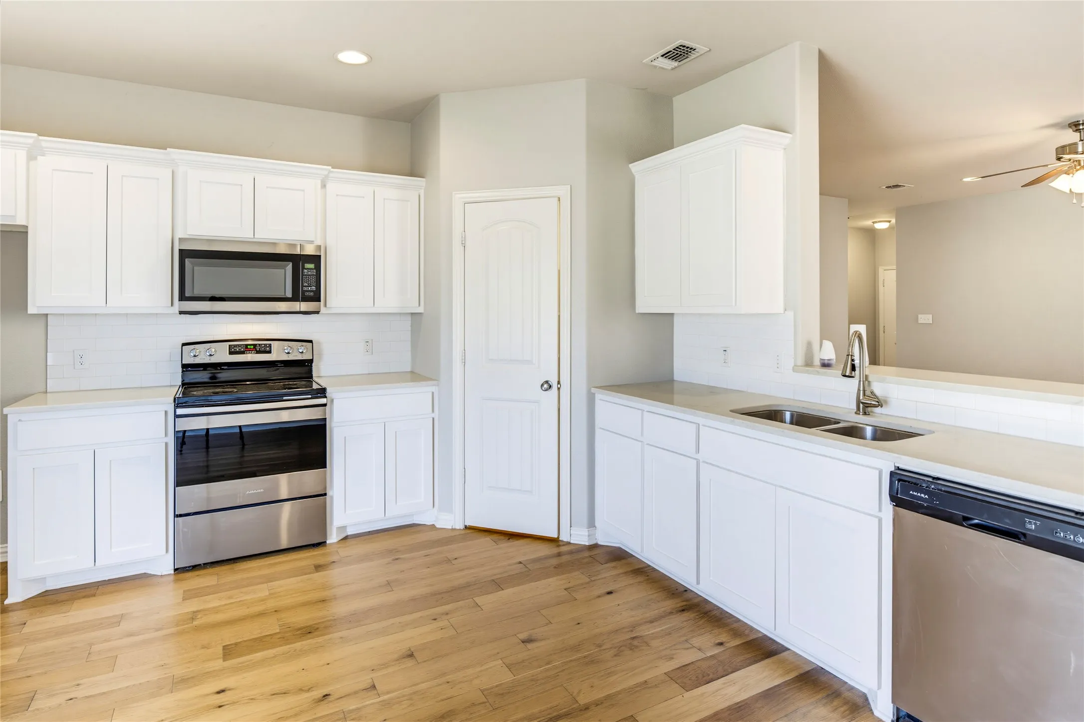 Kitchen featuring white cabinetry, wood-finish flooring, stainless steel appliances, a double basin sink, and solid surface countertops