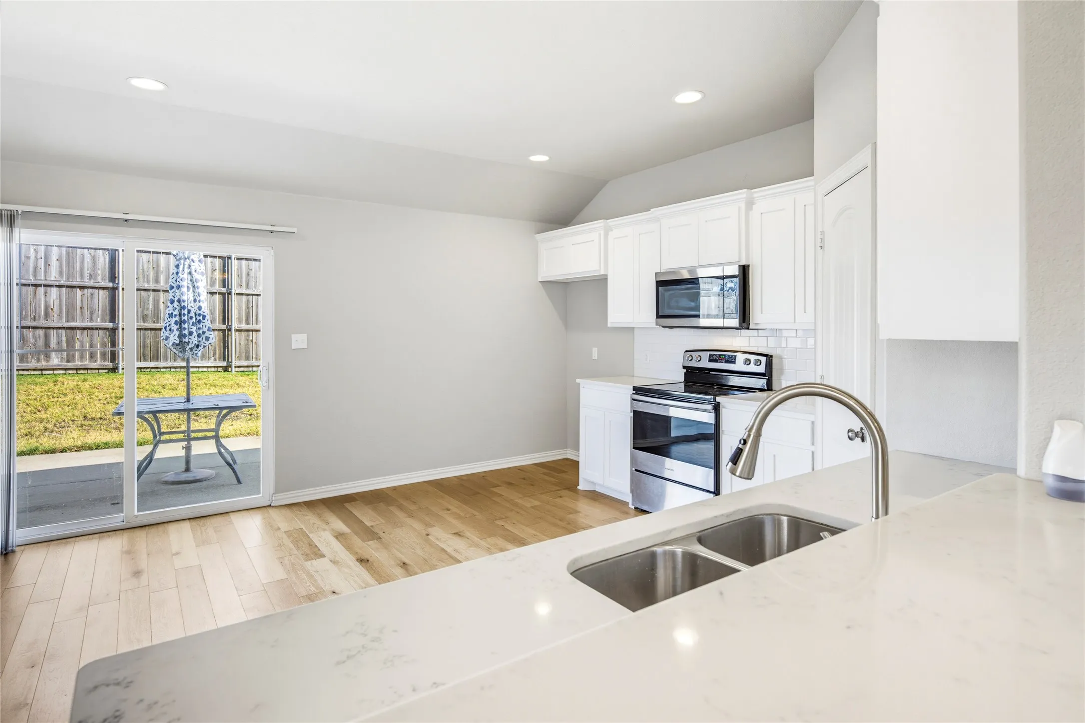 Kitchen featuring white cabinetry, stainless steel appliances, a double basin sink with a gooseneck faucet, and light wood-finish flooring