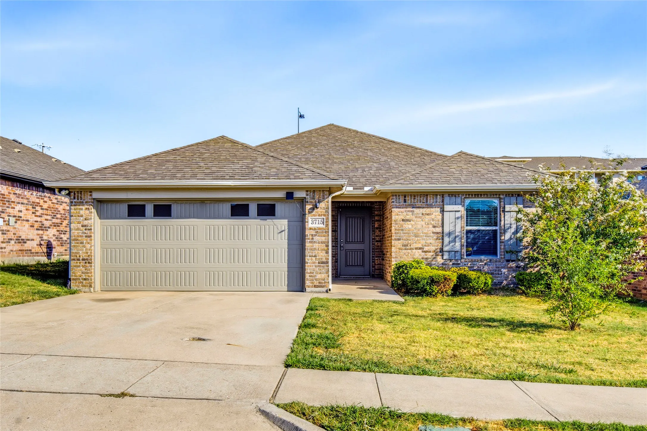 Brick exterior with stone accents, attached two-car garage, concrete driveway, front entry door, and a shingle roof