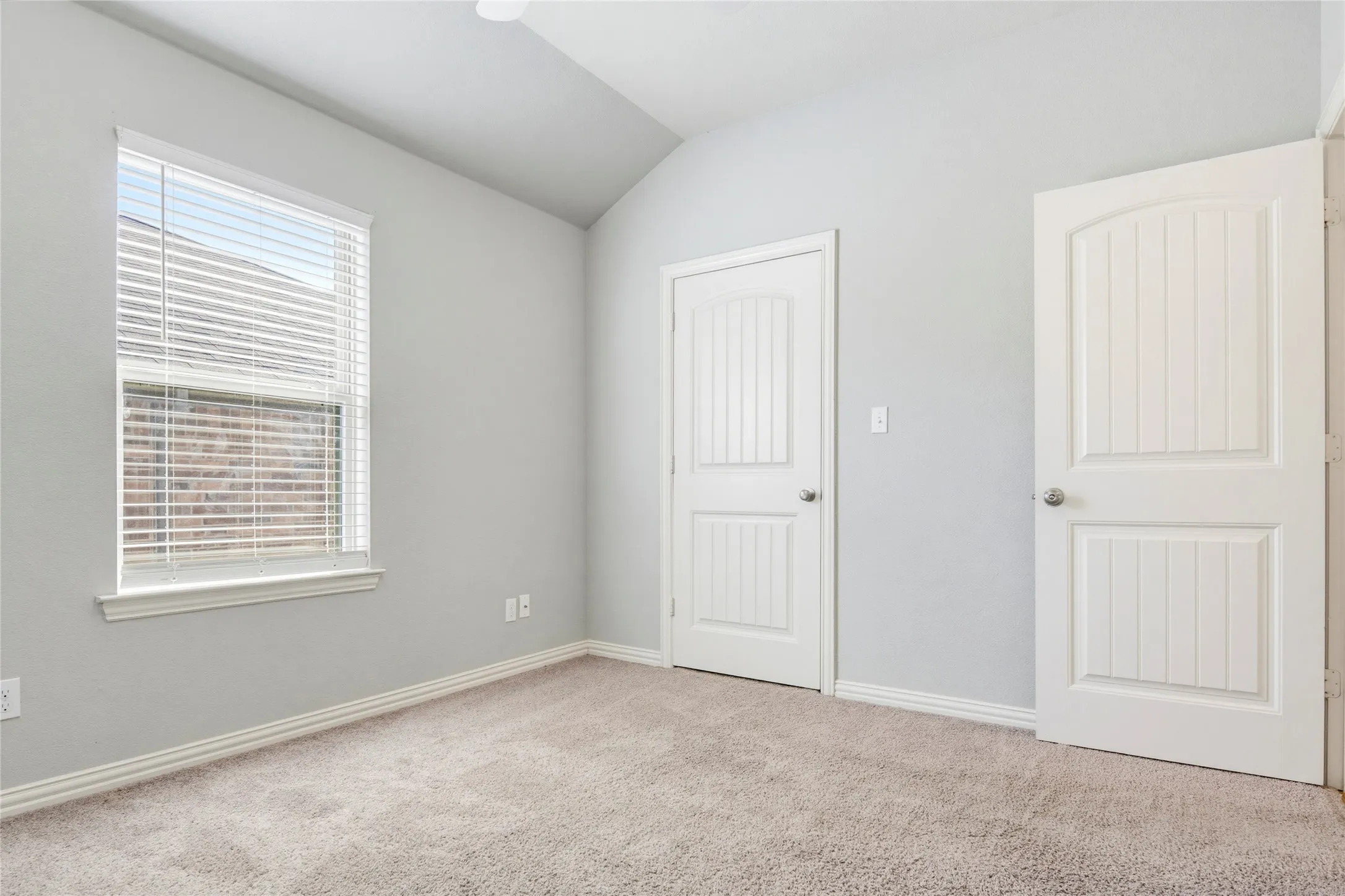 Vaulted ceiling with a ceiling fan, neutral carpet flooring, white window trim, and two white paneled doors with chrome hardware