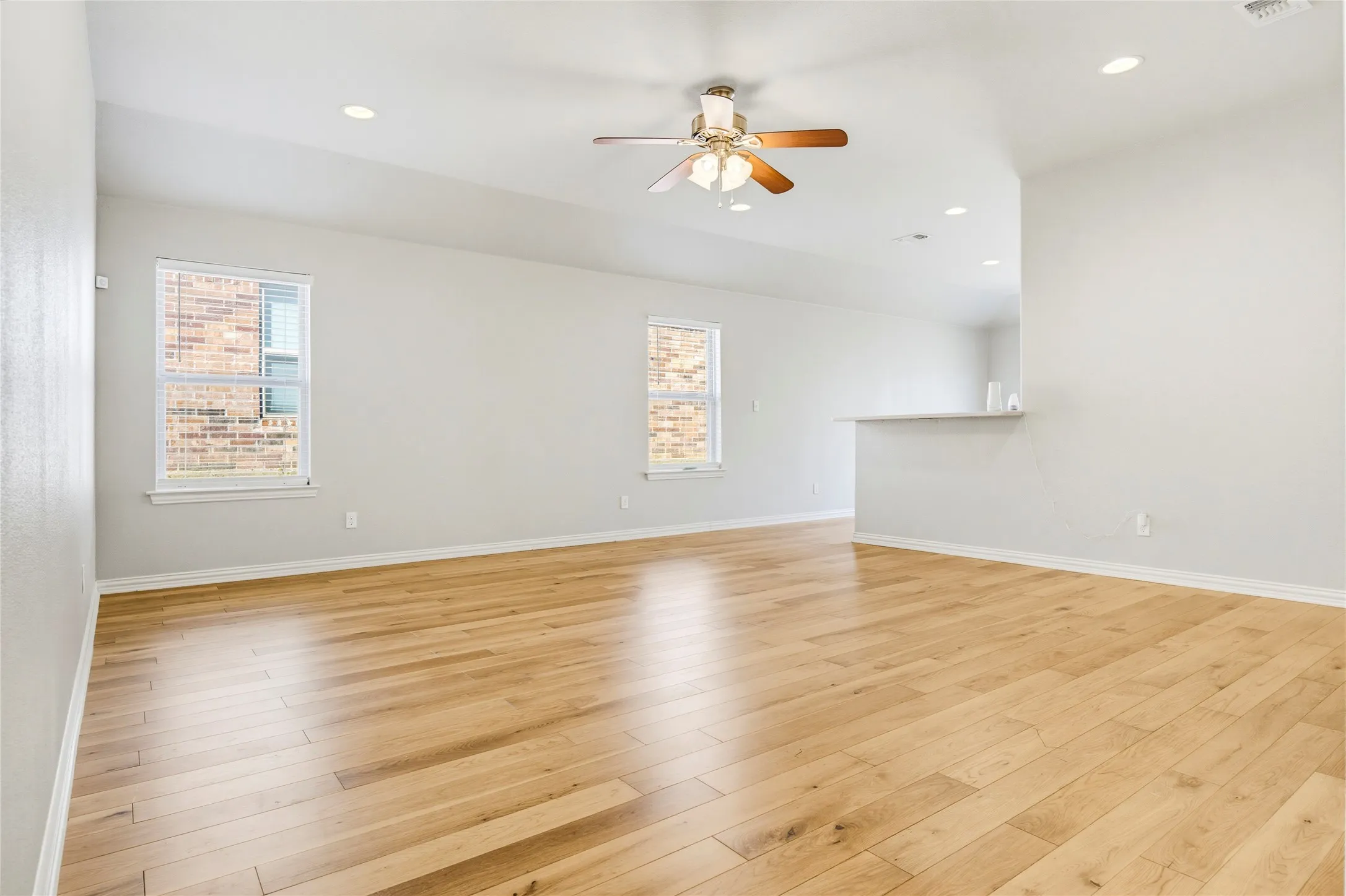 Open-concept living area featuring wood-finish flooring, recessed lighting, a ceiling fan, and two windows with blinds