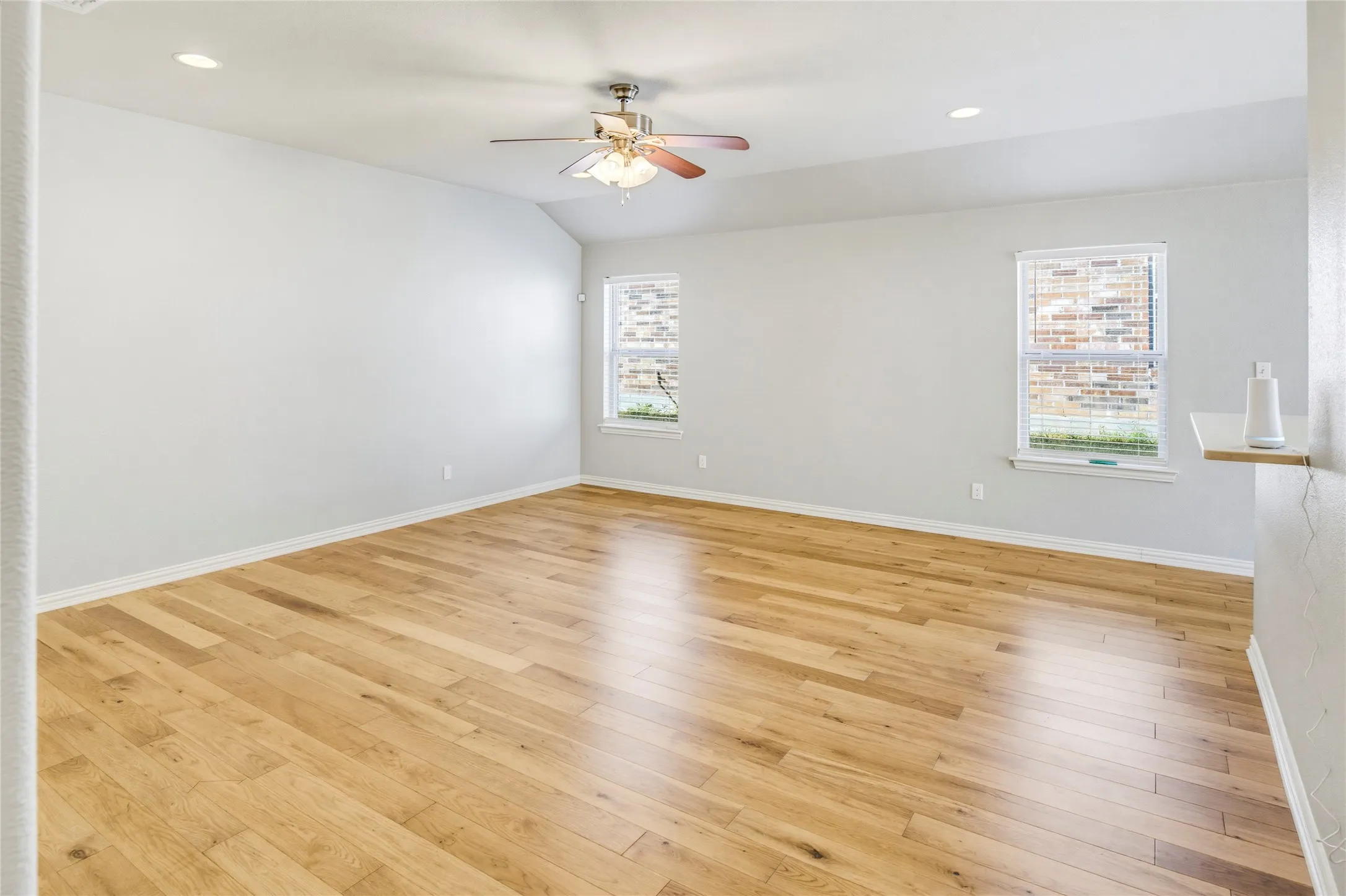 Vaulted ceiling with recessed lighting, wood-finish flooring, two windows with blinds, and a ceiling fan