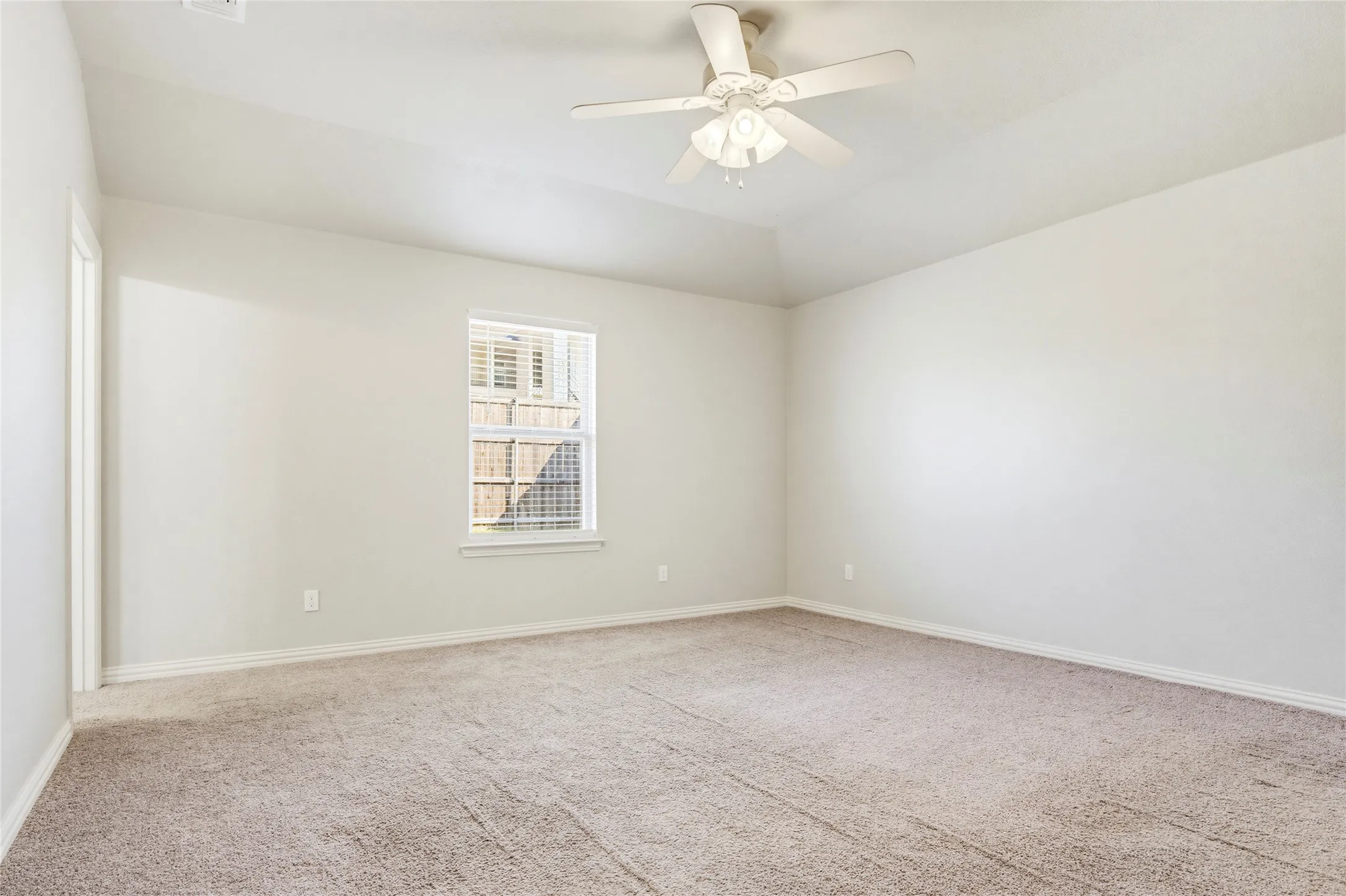 Neutral-toned carpet flooring, a vaulted ceiling, a ceiling fan with integrated lighting, and a double-hung window with blinds