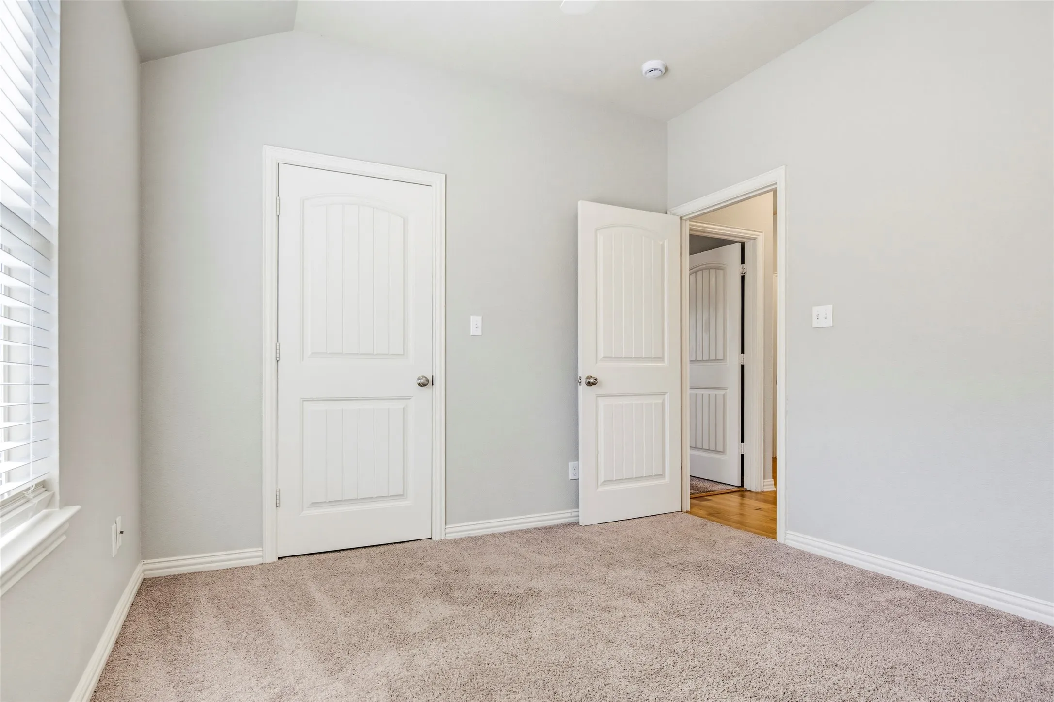 Vaulted ceiling, neutral wall paint, carpet flooring, white paneled doors, and window with blinds