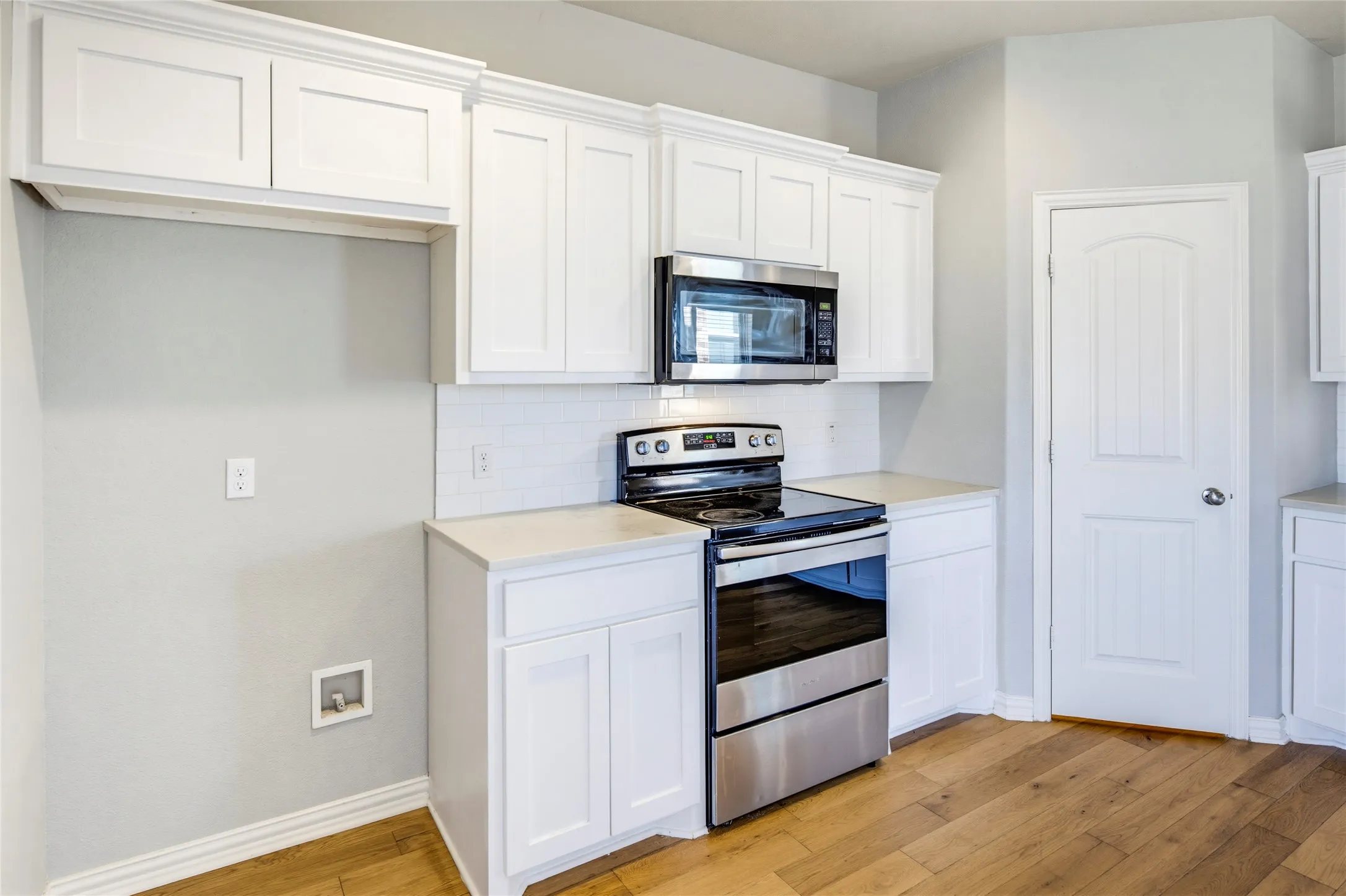 White shaker-style cabinetry with crown molding, stainless steel microwave, stainless steel range, light-toned countertops, and wood-finish flooring