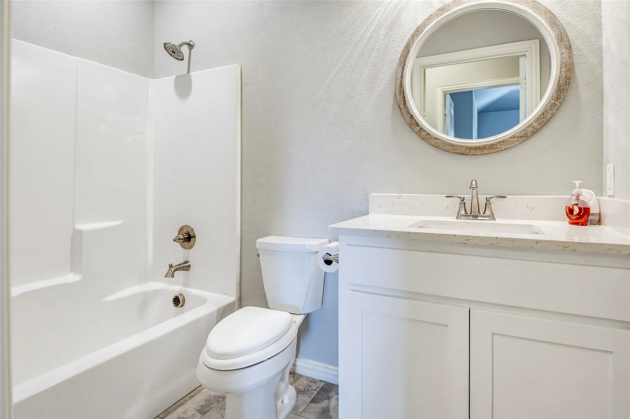Bathroom featuring a tub and shower combination with brushed nickel fixtures, a single vanity with shaker-style cabinetry, a white countertop, and a circular mirror