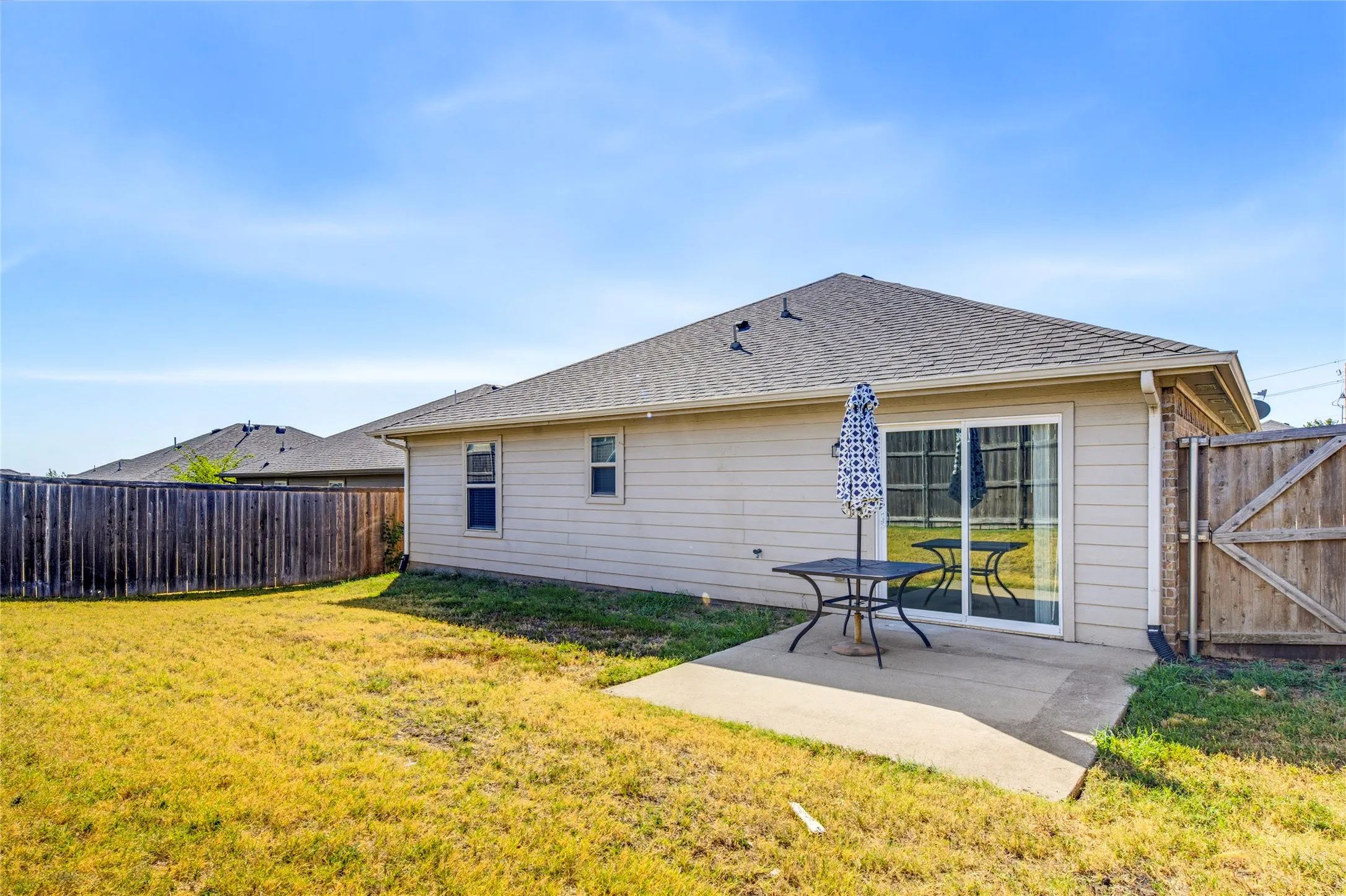 Expansive backyard featuring a concrete patio, sliding glass door, and wood privacy fencing