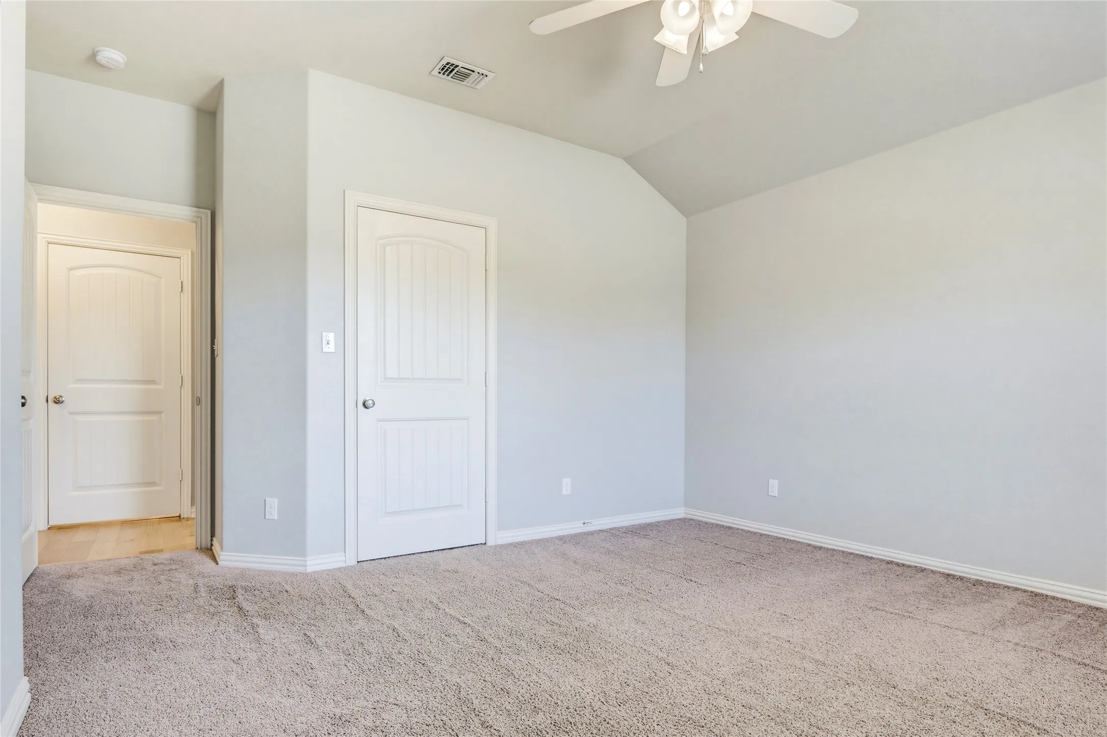Vaulted ceiling with a ceiling fan, light-colored carpeting, two paneled doors, and light gray wall finishes
