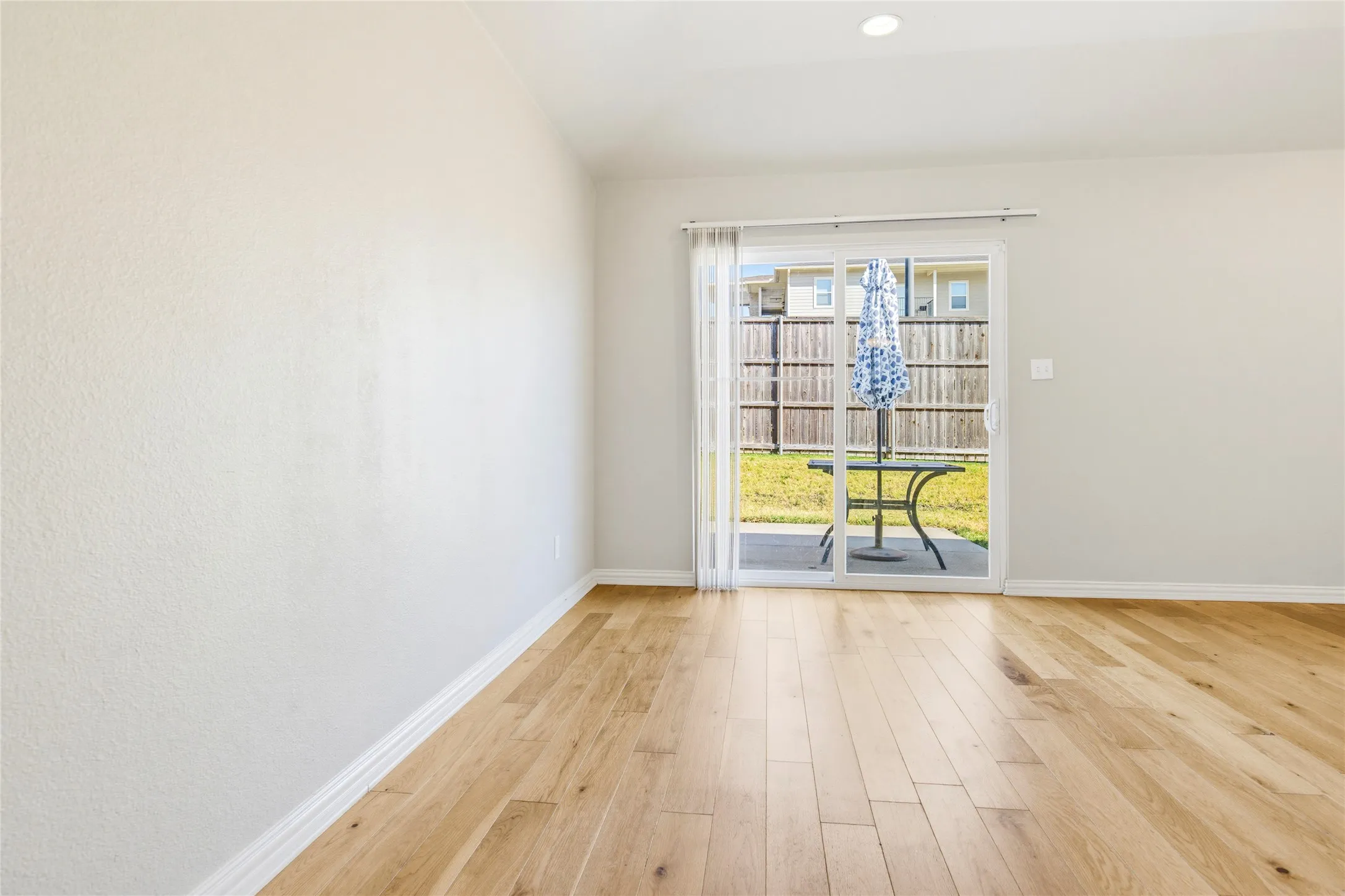 Wood-finish flooring, light-toned walls, recessed ceiling lighting, and sliding glass door to a concrete patio and fenced backyard