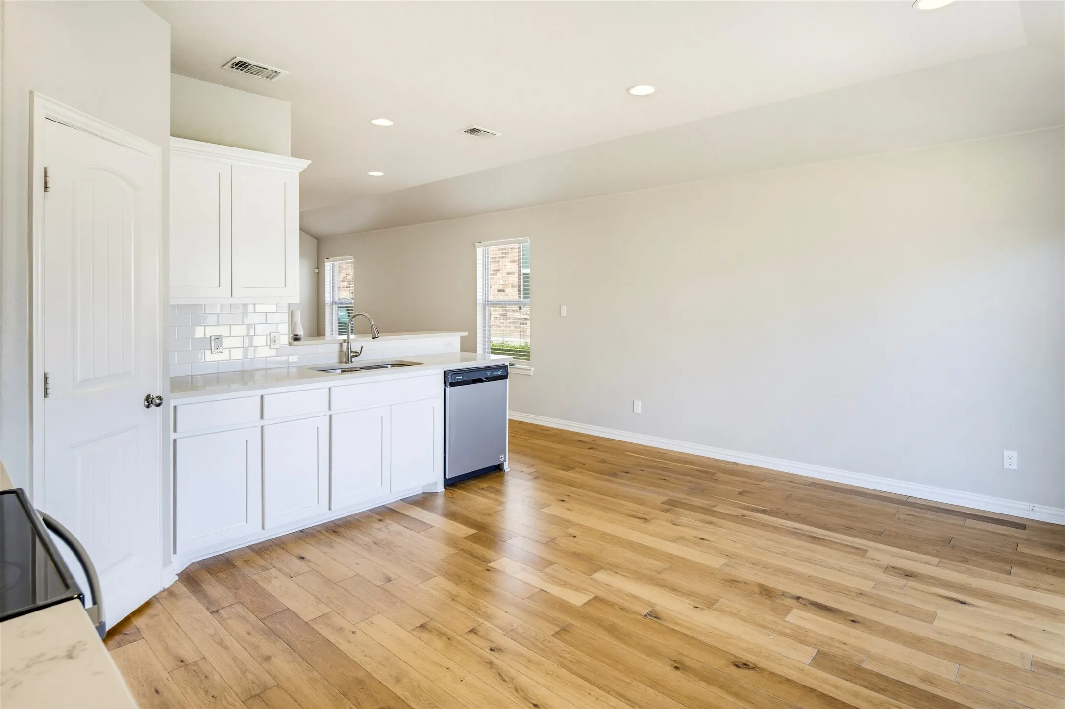 Kitchen with white cabinetry, subway tile backsplash, stainless steel dishwasher, and wood-finish flooring