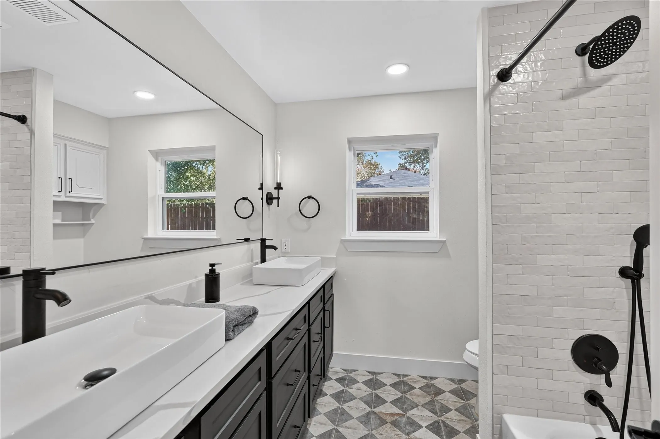 Dual vessel sinks set on a long vanity with dark cabinetry, featuring a full-width mirror