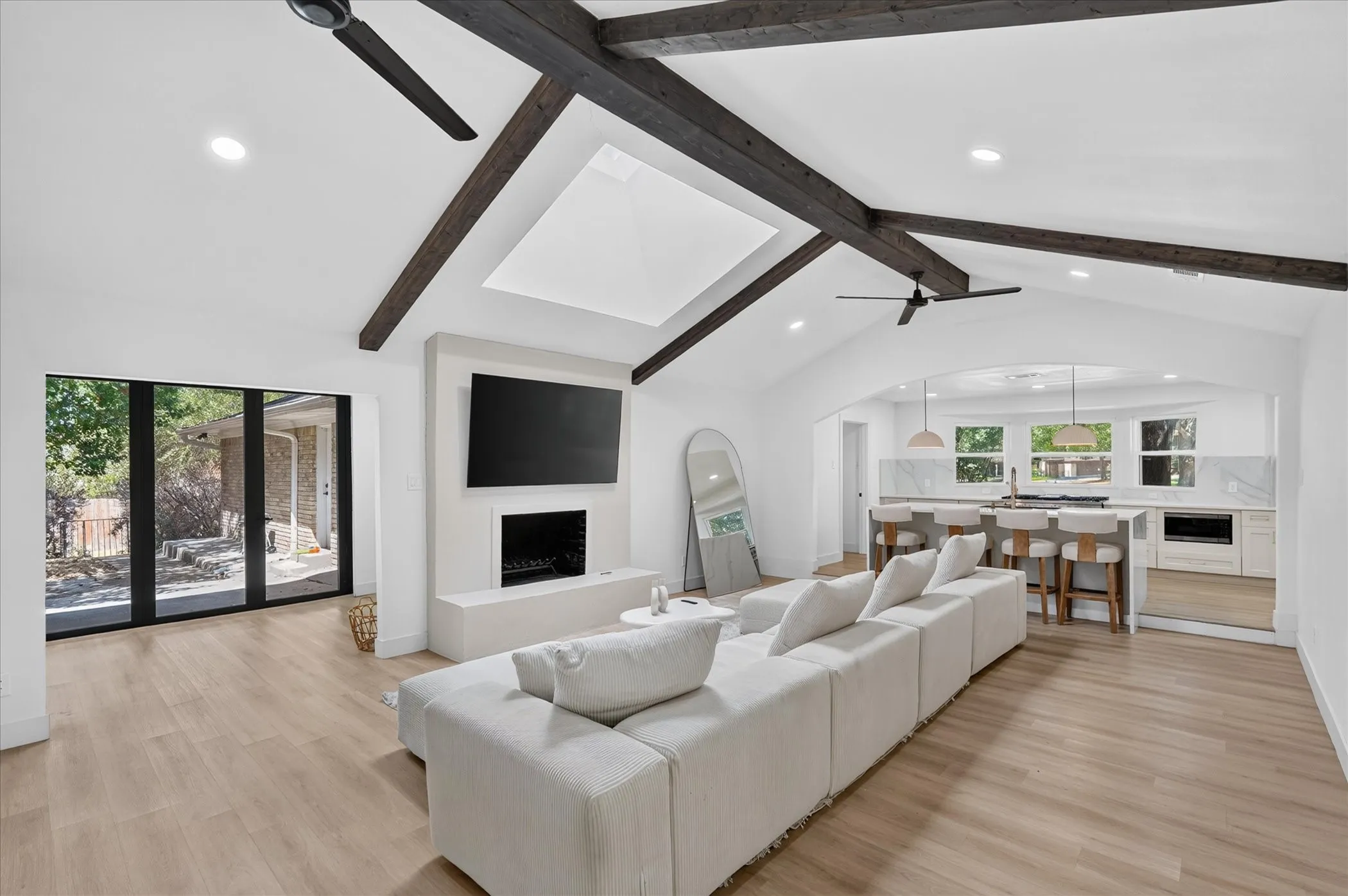 Vaulted ceilings with exposed beams, built-in fireplace, recessed lighting, wood-finish flooring, and large glass doors