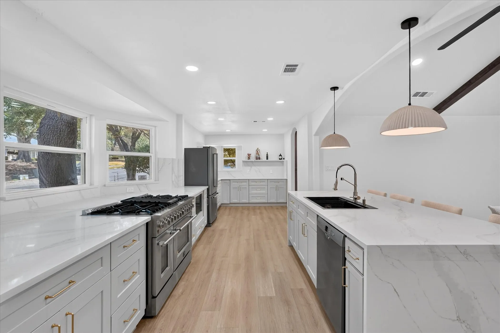 Spacious kitchen featuring an extended center island, integrated sink, light wood-finish flooring, and light gray cabinetry