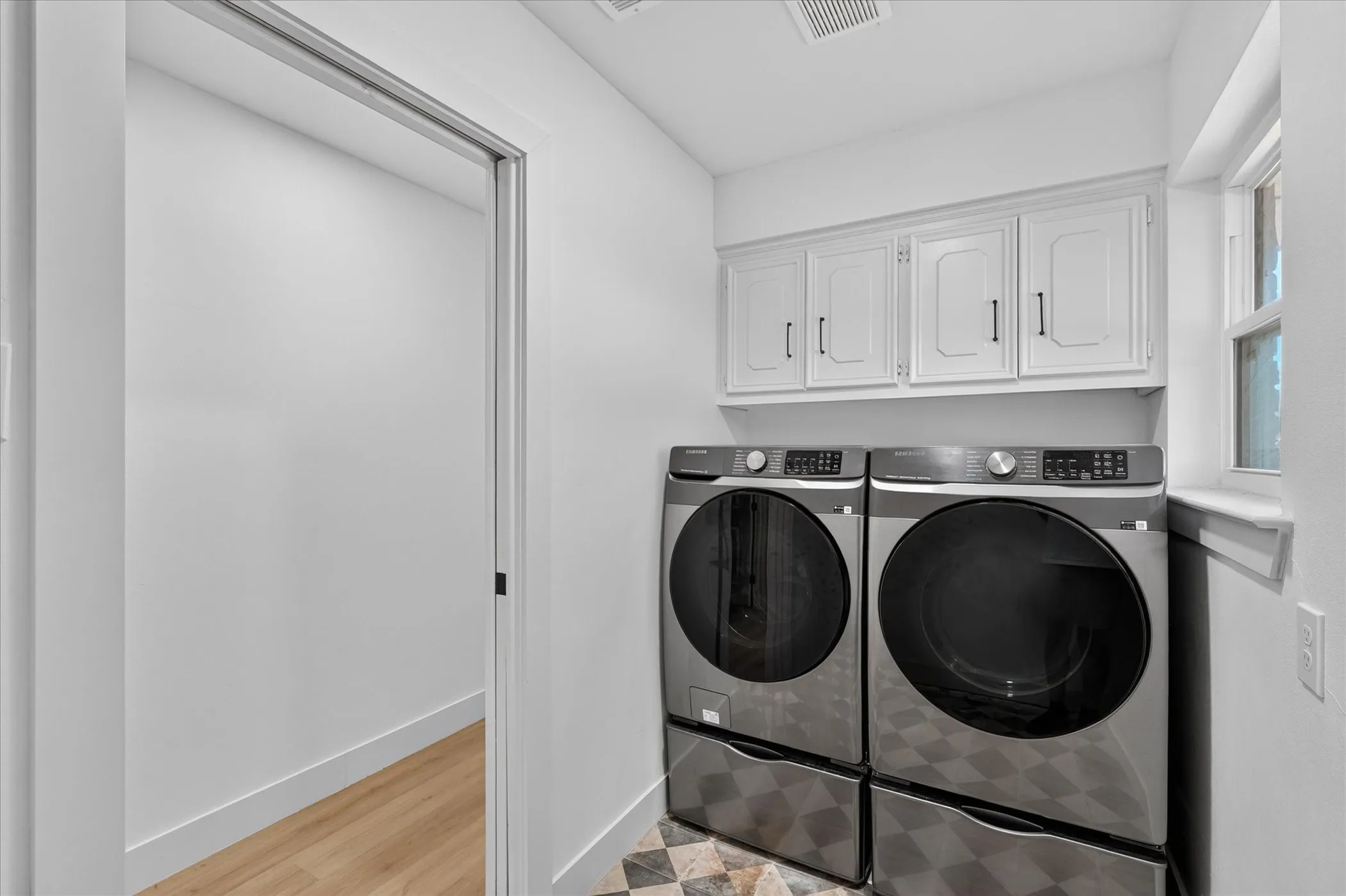 Laundry area featuring white cabinetry, a window, and checkered floor tiling
