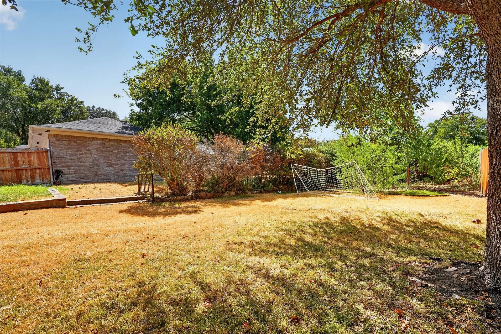 Expansive backyard featuring mature trees, wood fencing, and a brick-sided exterior