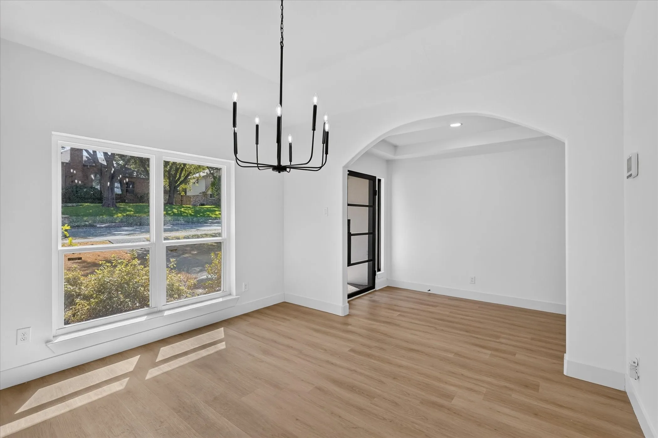 Spacious room with wood-finish flooring, a contemporary chandelier, large windows, and an arched entry