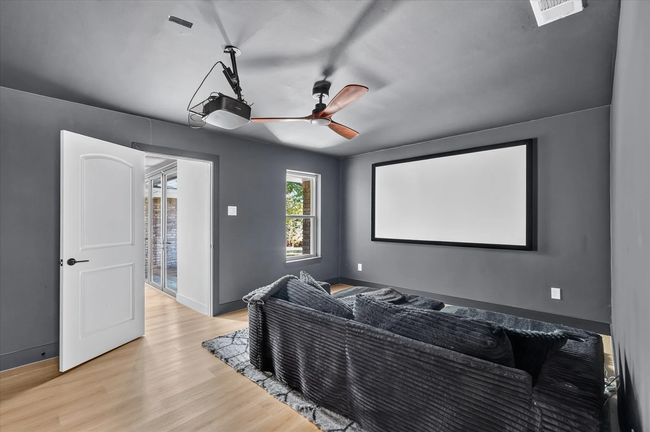 Dedicated media room with a wall-mounted projection screen, ceiling-mounted projector, and a ceiling fan