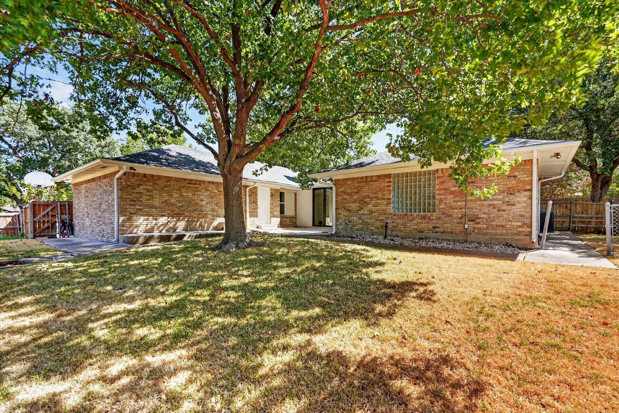 Expansive backyard with a mature tree, brick exterior, and a privacy fence