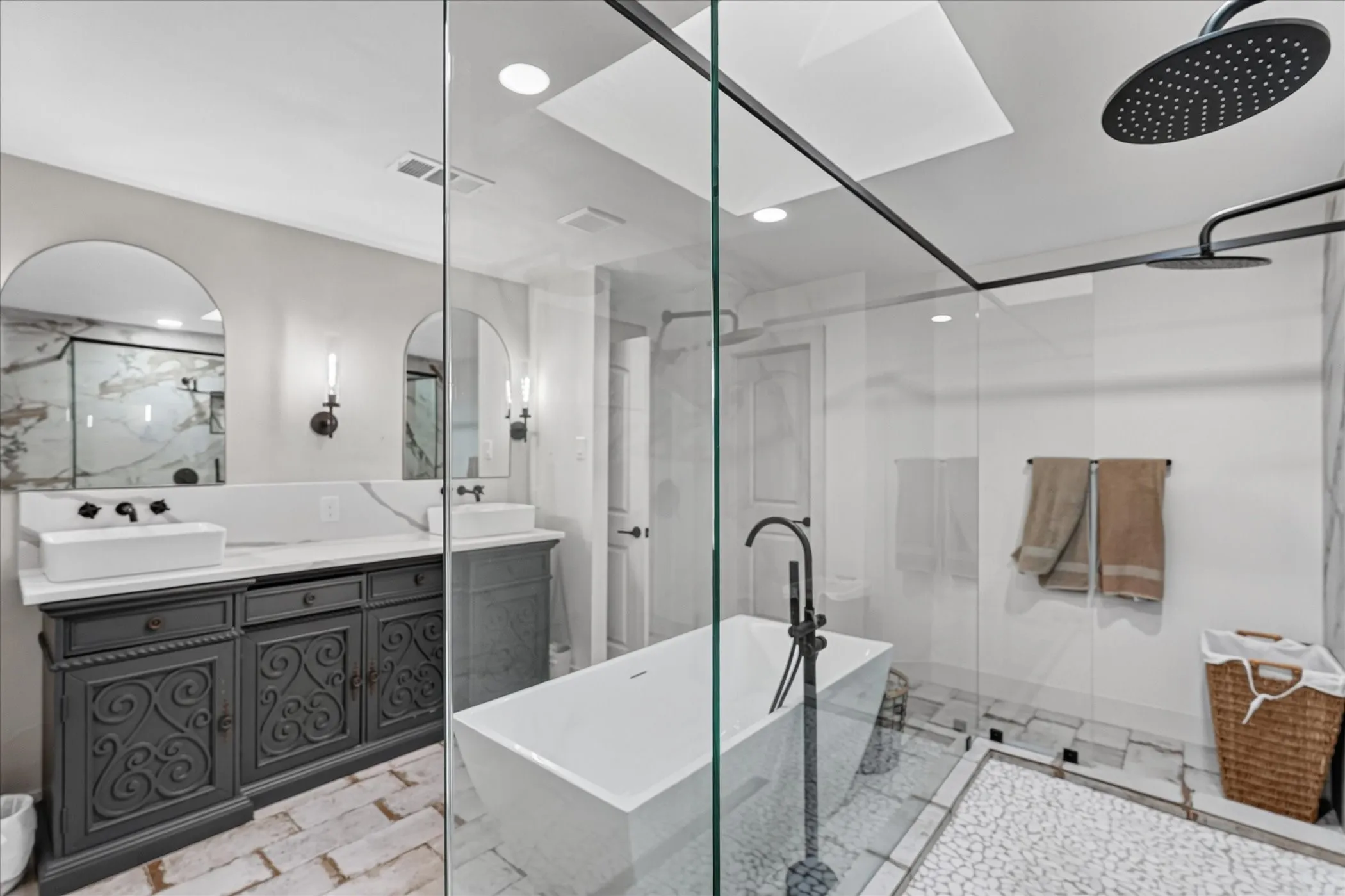 Dual vanity with vessel sinks, freestanding soaking tub, frameless glass shower enclosure, black matte fixtures, and skylights